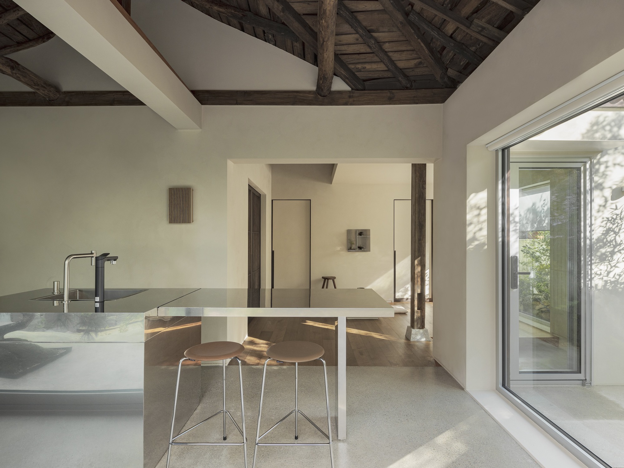 Kitchen island with bar seating beneath exposed timber roof trusses and afternoon sunlight