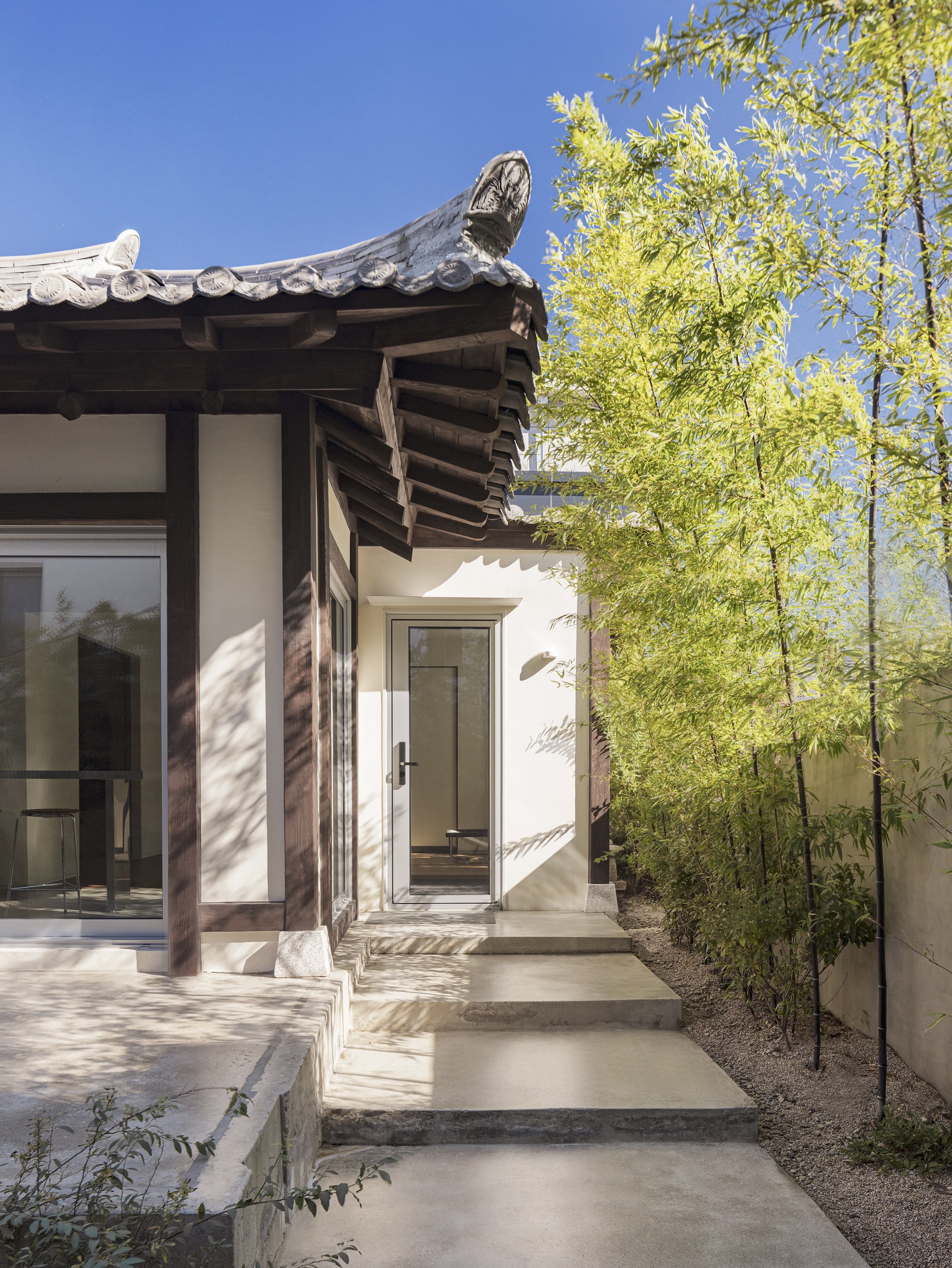 Entry sequence with timber columns and tiled eaves beside tall bamboo in clear daylight