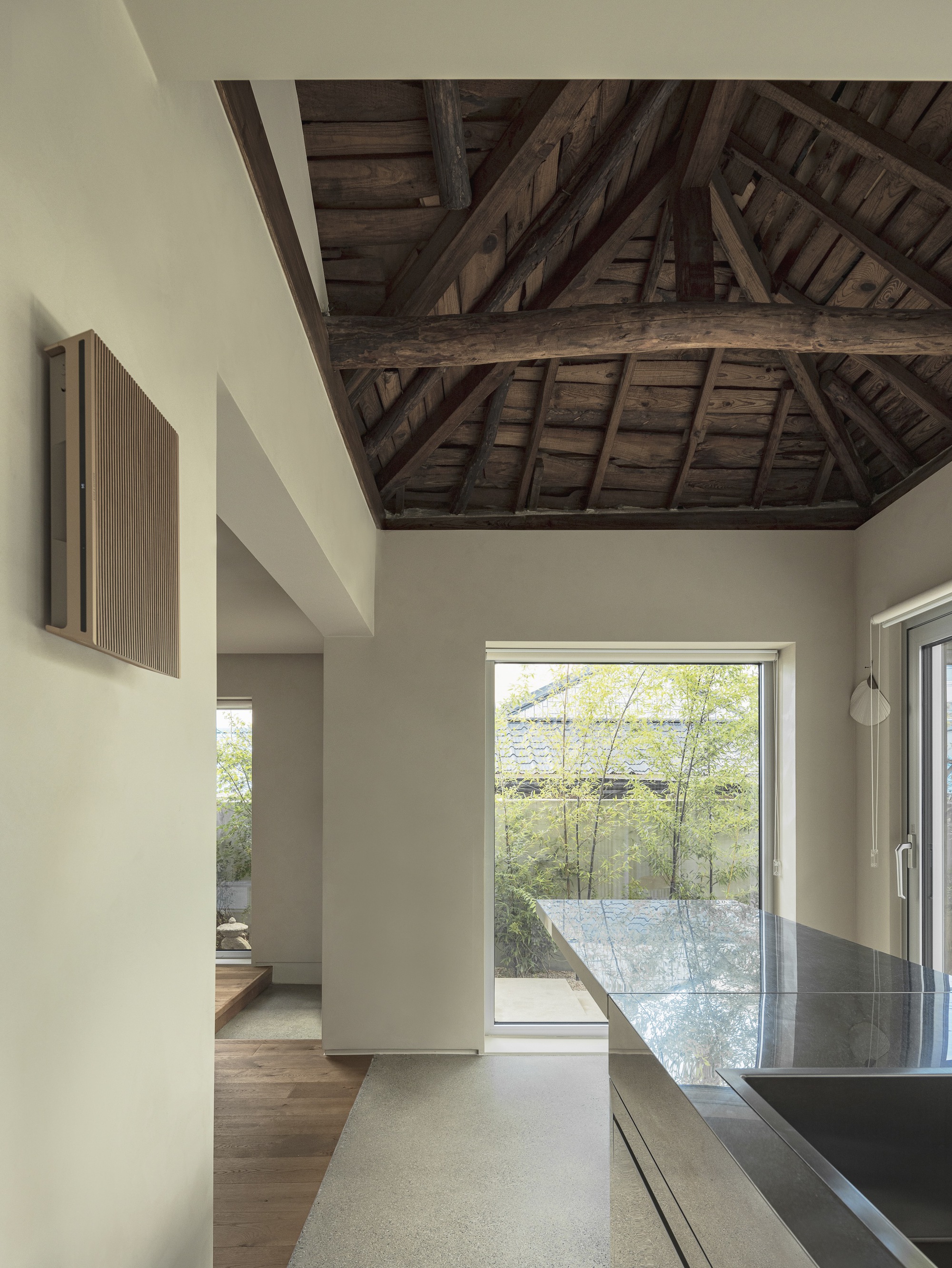 Kitchen interior with exposed timber roof structure and window framing a gravel courtyard with bamboo