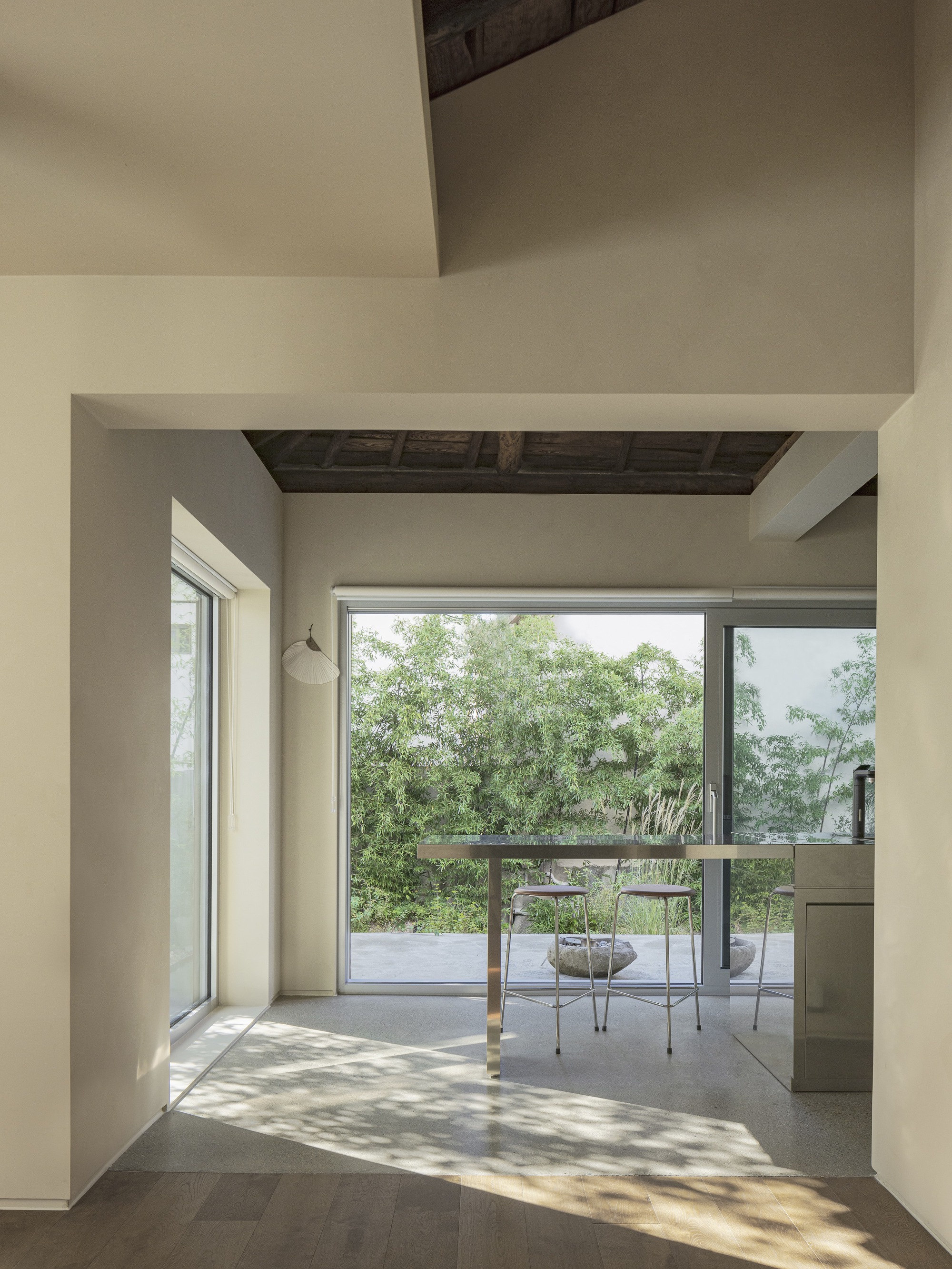 Interior corridor with dappled sunlight leading toward a glass-walled terrace and dining area
