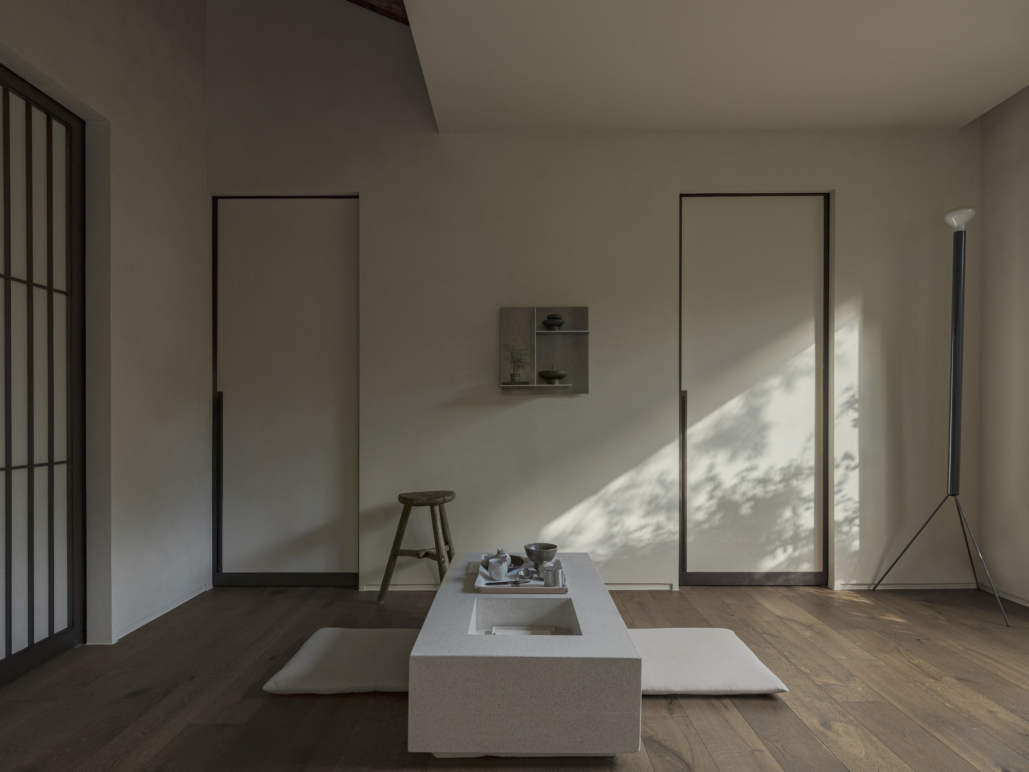 Minimalist interior with flush panel doors, low stone platform and dappled sunlight across oak floors