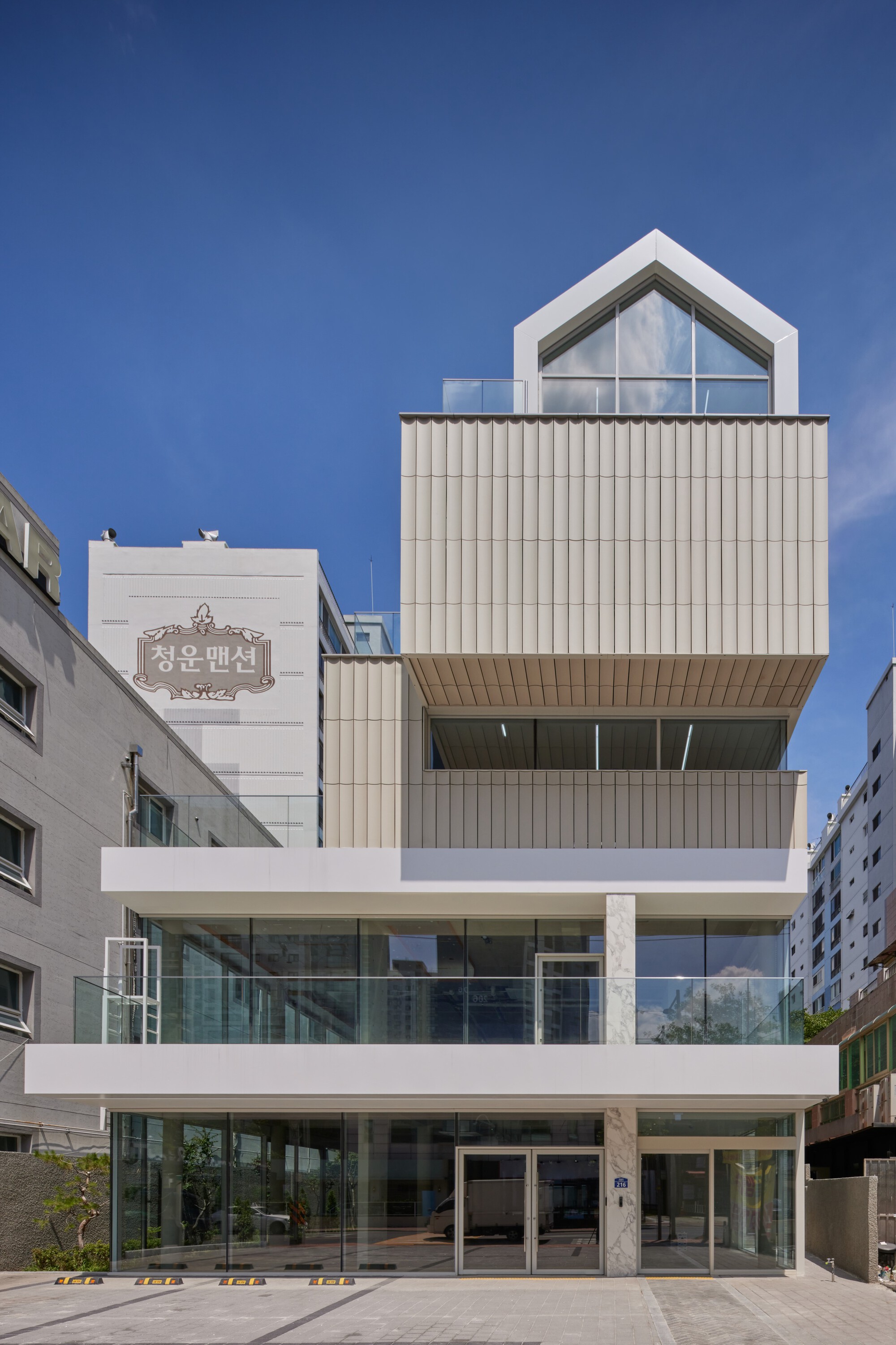 Street facade with stacked volumes of corrugated metal panels and glazed lower levels under clear sky