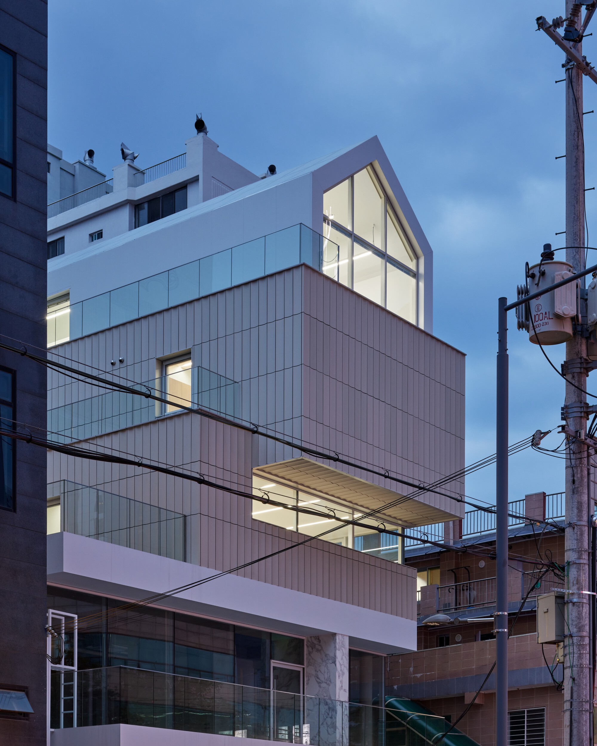 Stacked facade with vertical ribbed cladding and illuminated interiors at dusk with overhead power lines