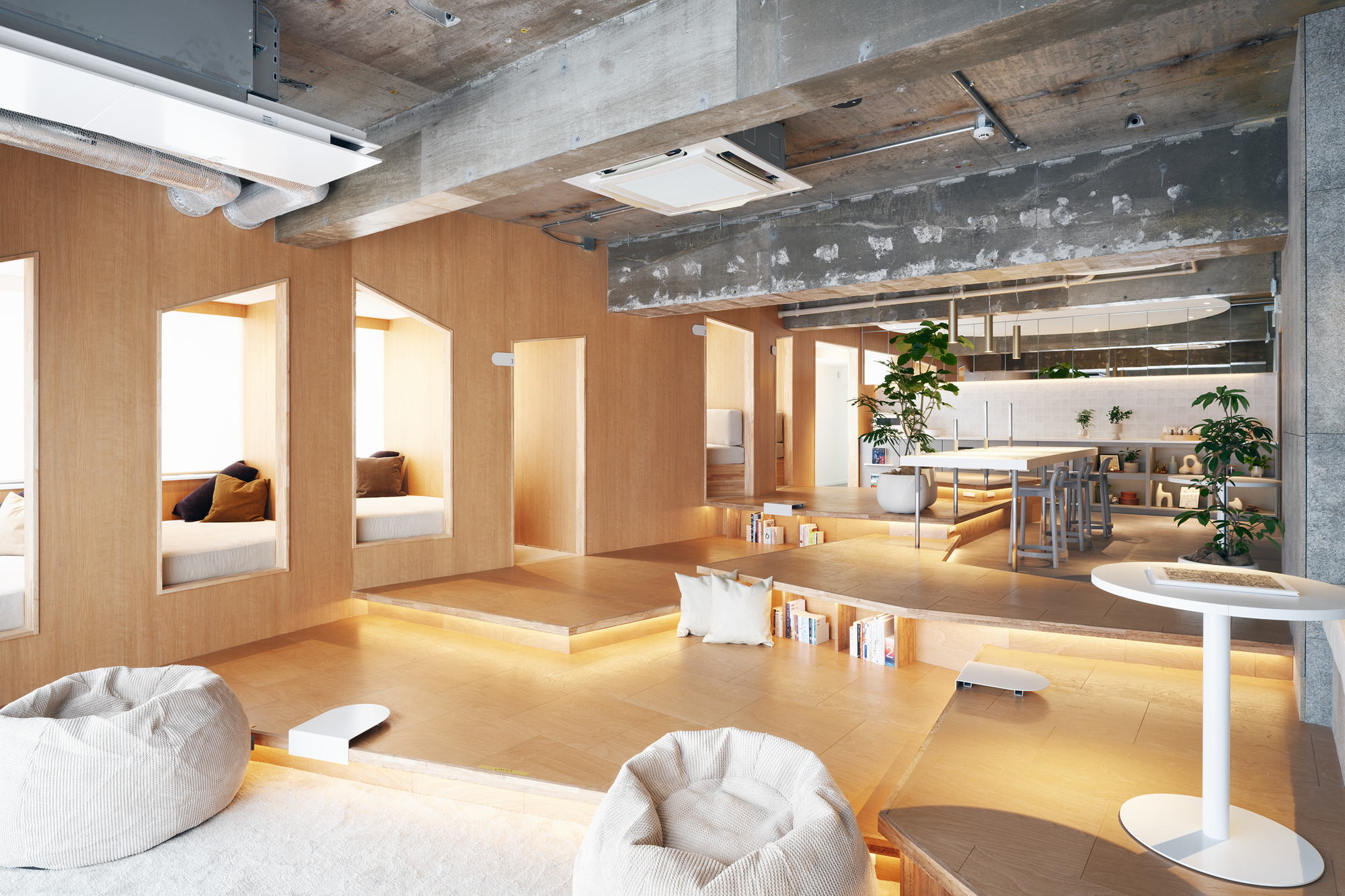 Open-plan interior with sunken plywood platform seating and exposed concrete ceiling beams