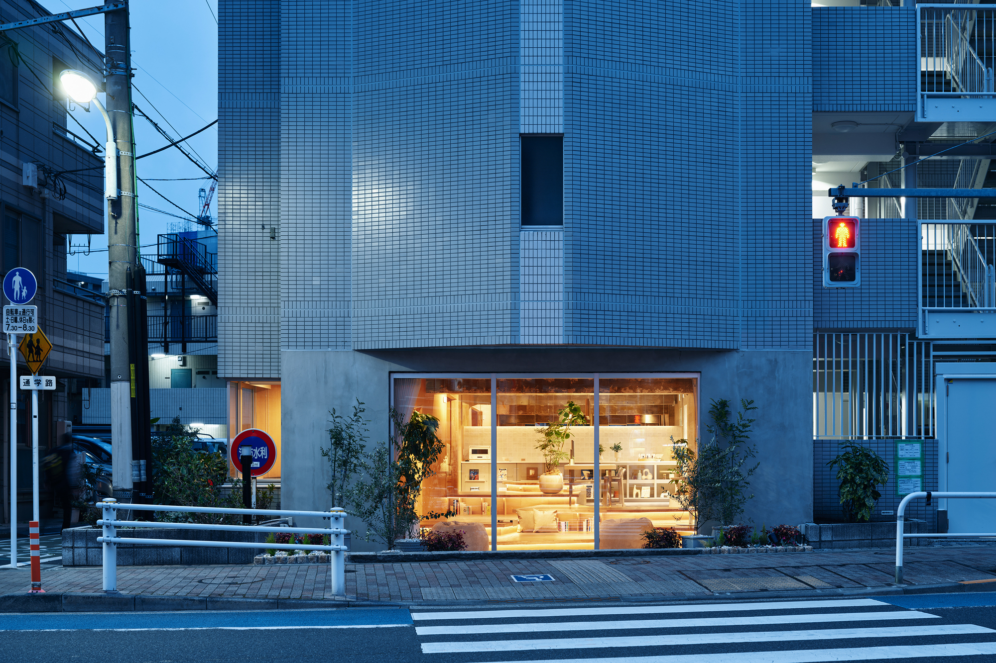 Street view of illuminated storefront with glass facade at dusk beside a crosswalk