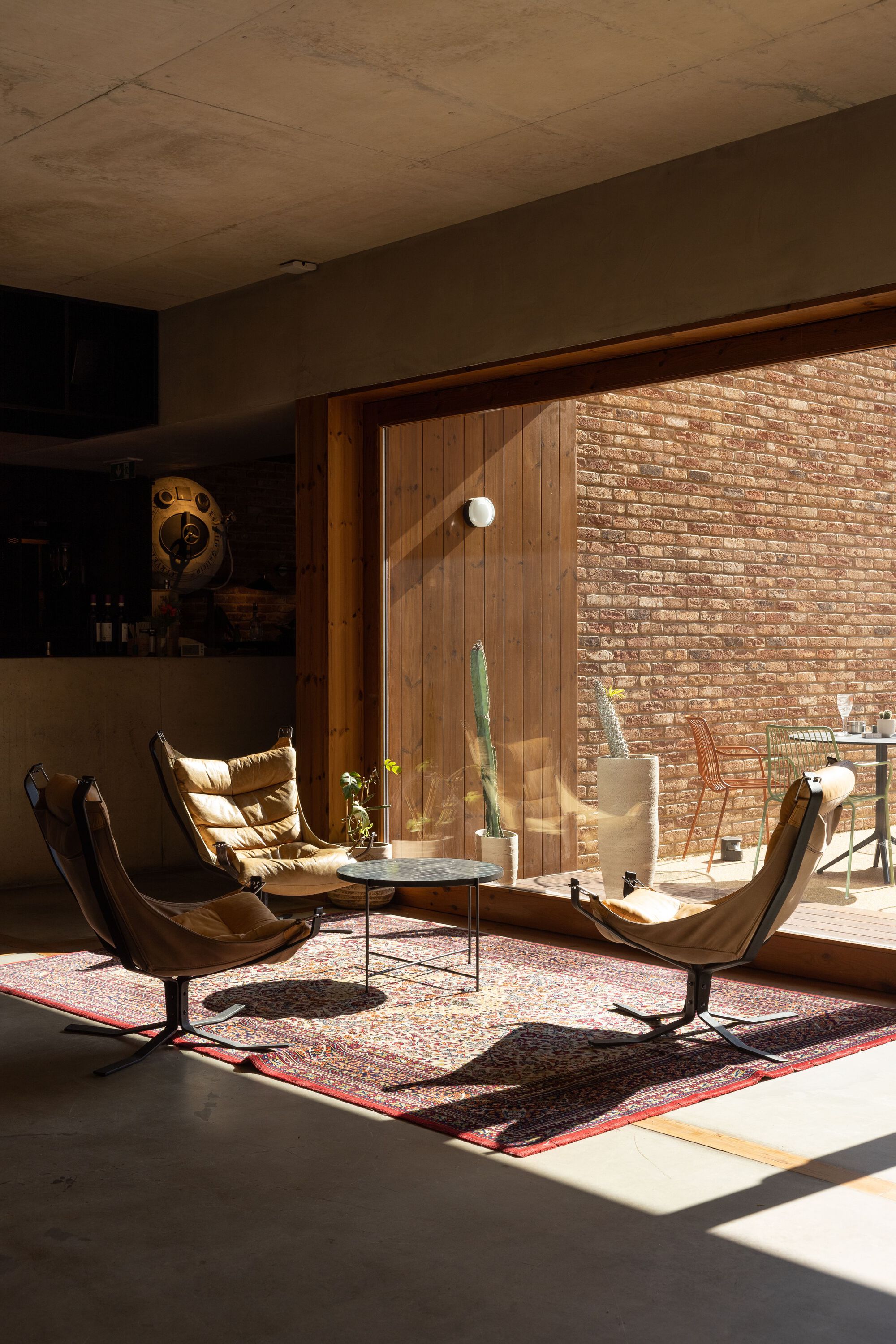 Living space with timber-clad glazing opening to a brick courtyard in afternoon sunlight