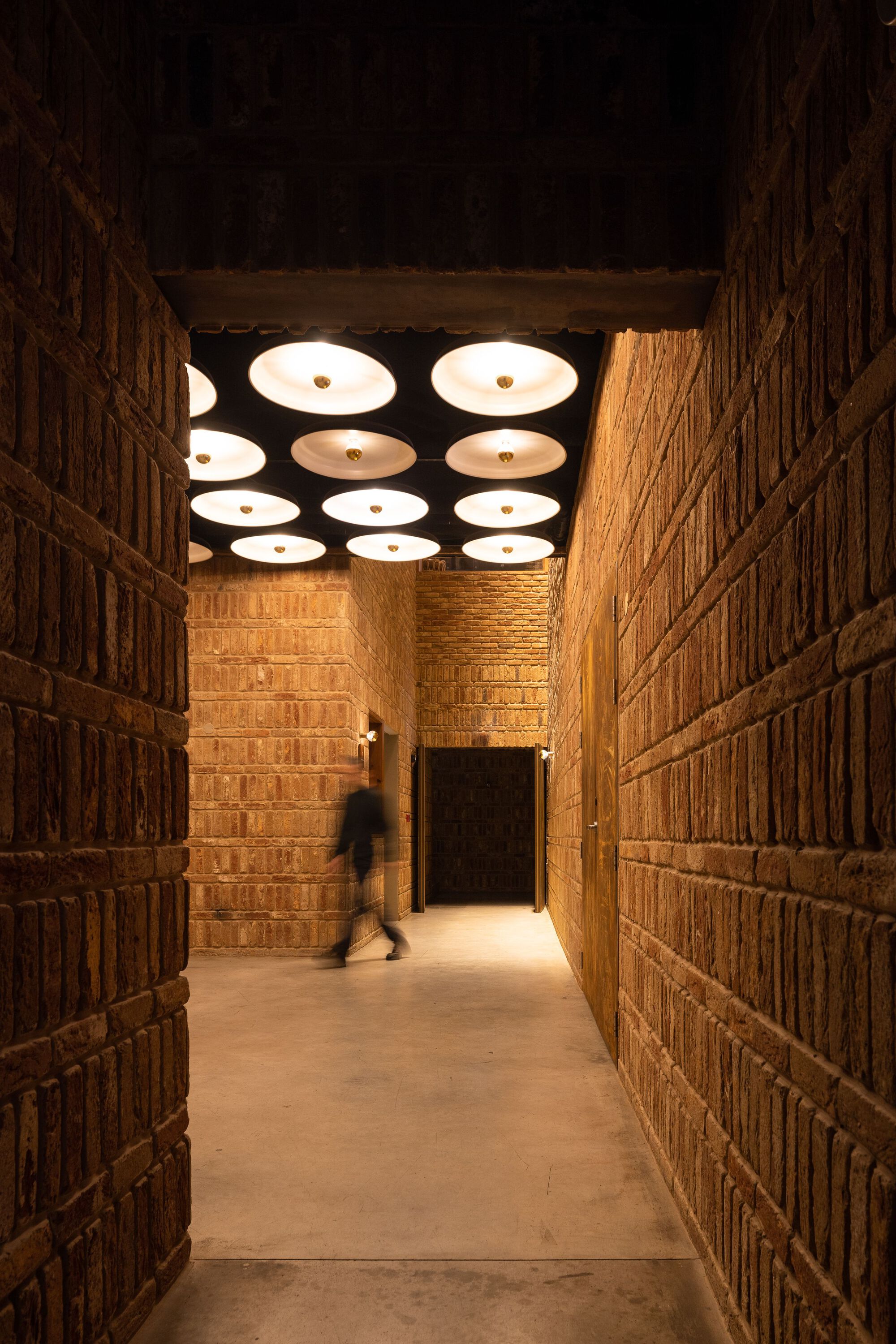 Corridor with textured brick walls and circular ceiling lights illuminating a figure passing through
