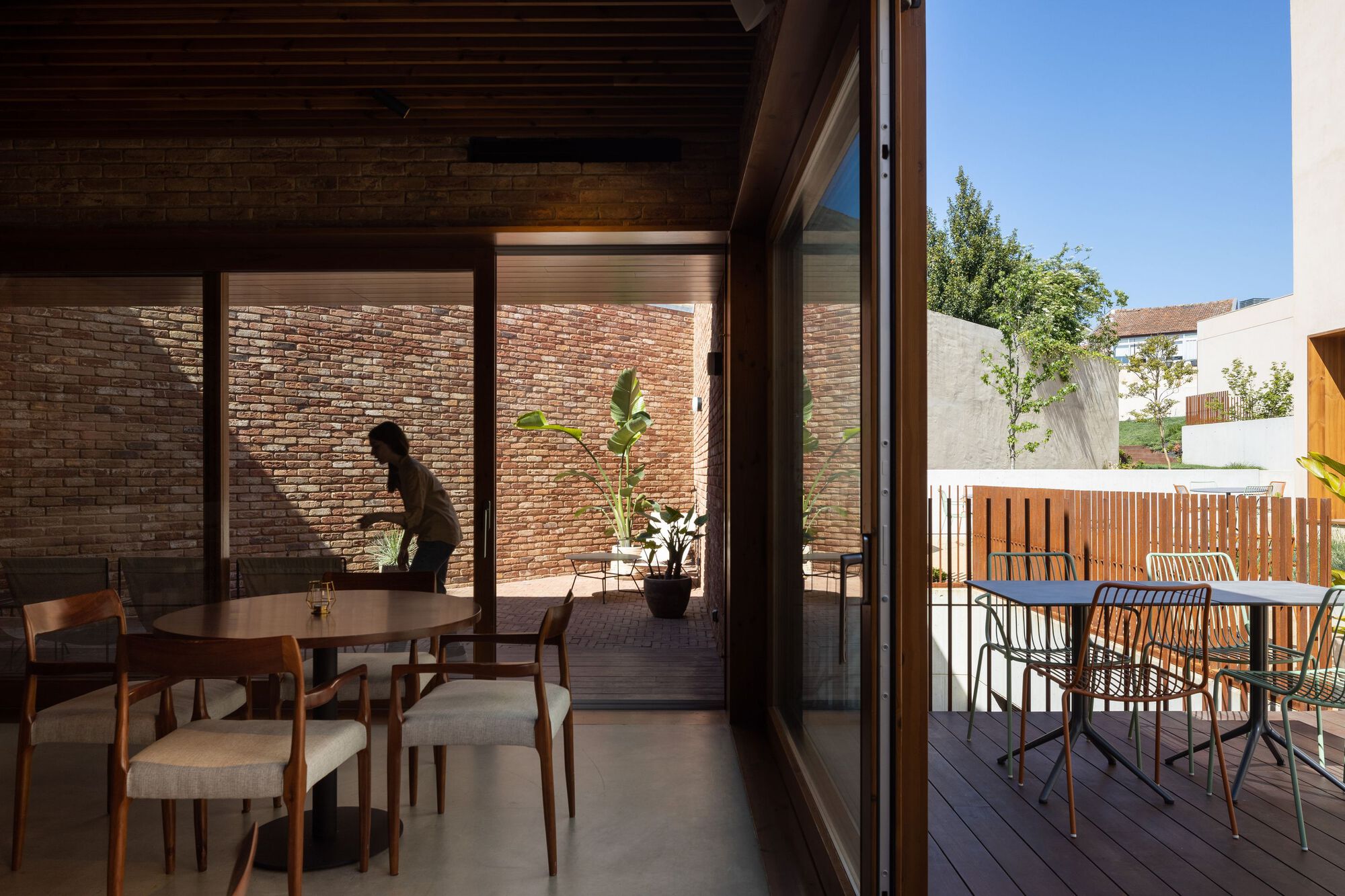 Dining area opening through glazed doors to a timber deck and brick courtyard wall
