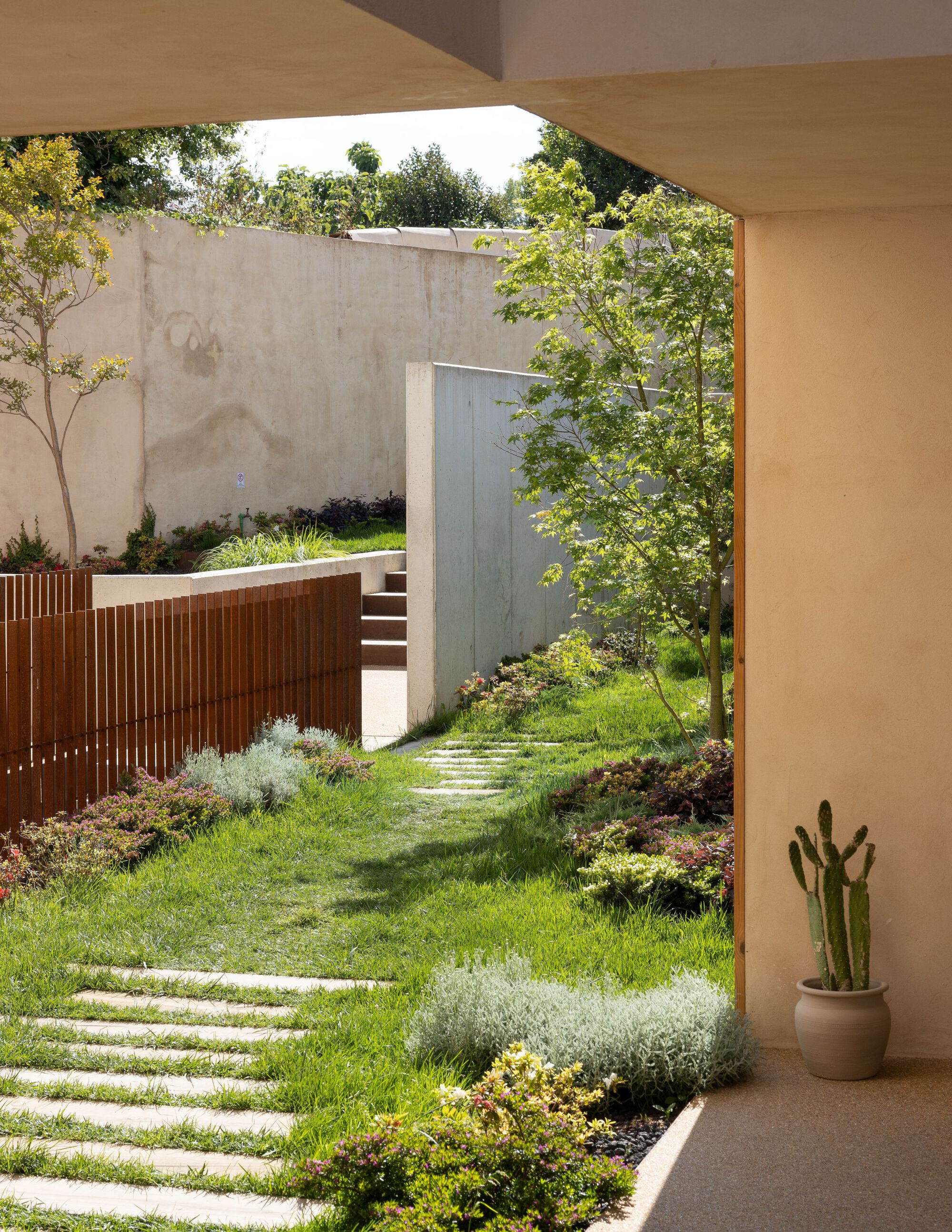 Garden courtyard view through arched opening with stepping stone path and timber slatted screen wall beyond