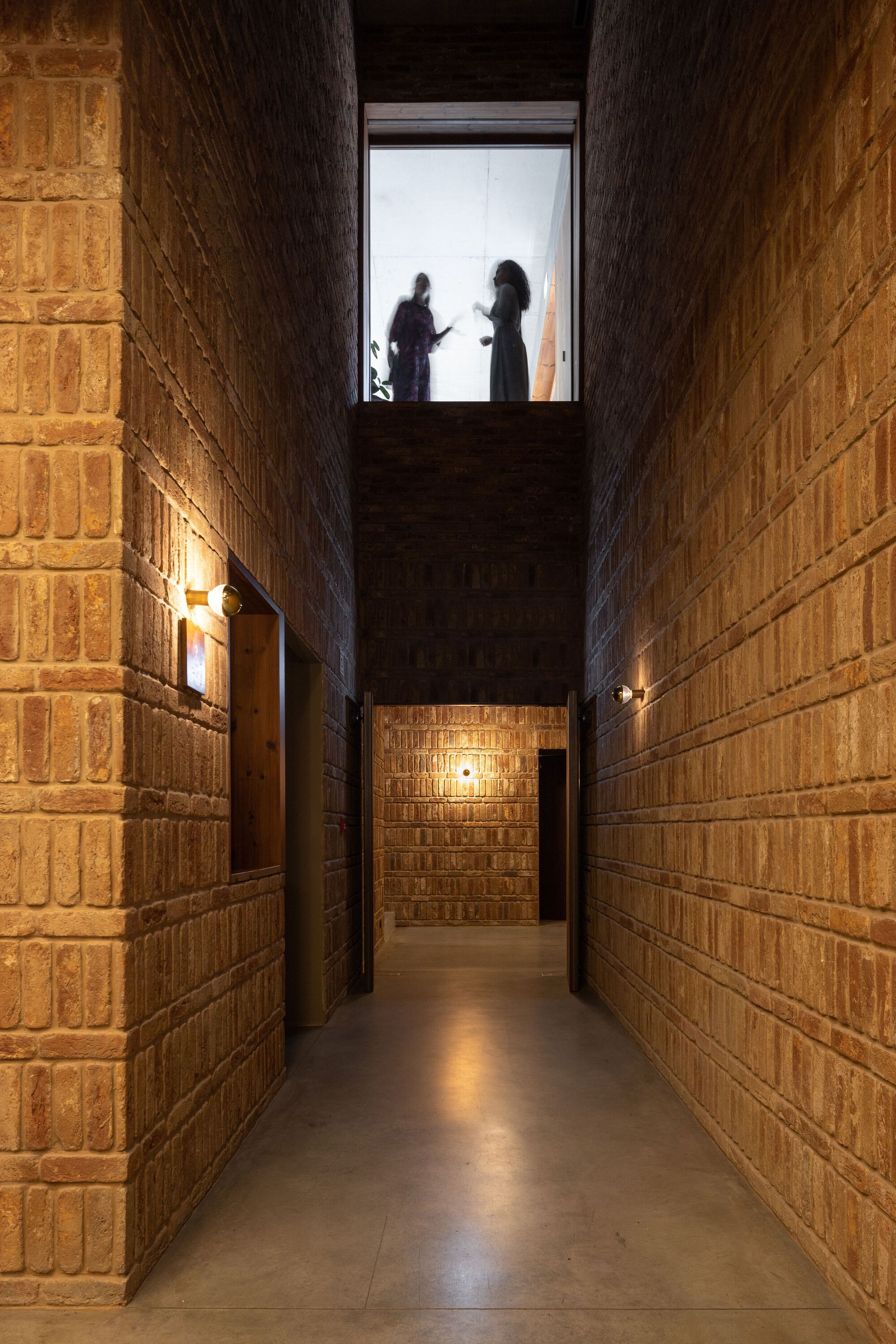Narrow corridor with brick walls and two figures silhouetted in the skylit opening above