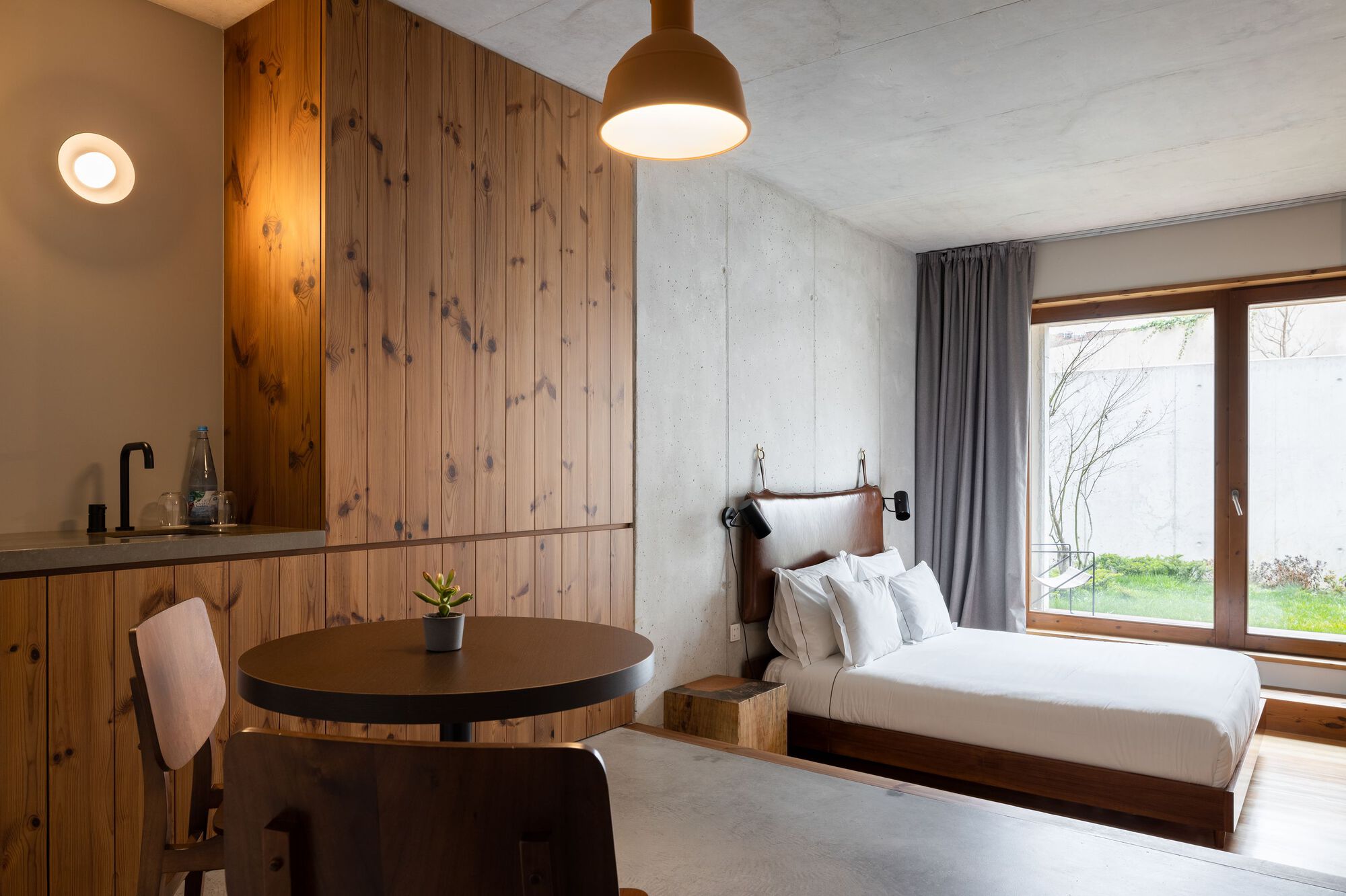 Guest room with knotty timber paneling, concrete ceiling and timber-framed window overlooking lawn