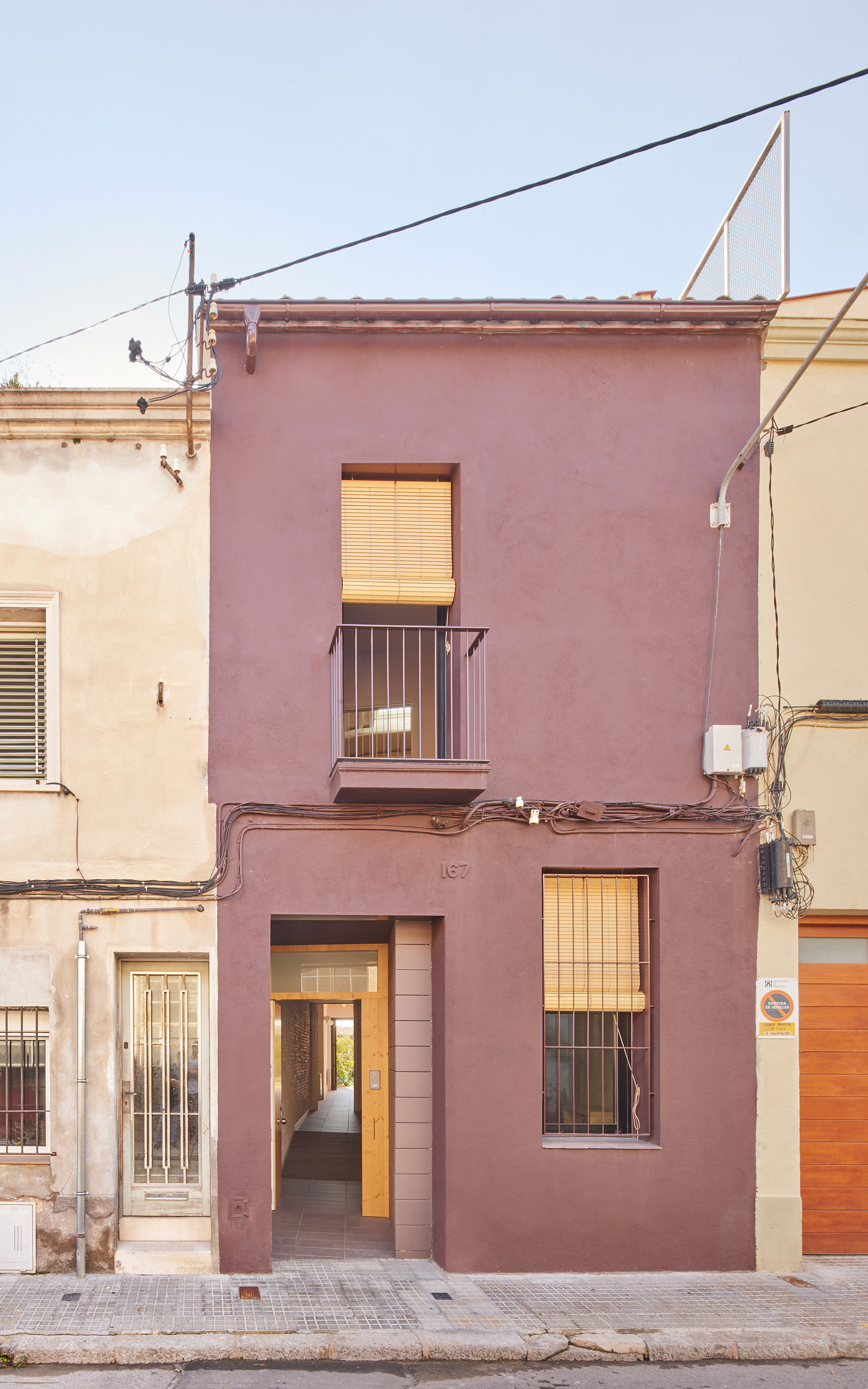 Street facade with mauve render, timber-screened openings and small balcony beneath overhead power lines