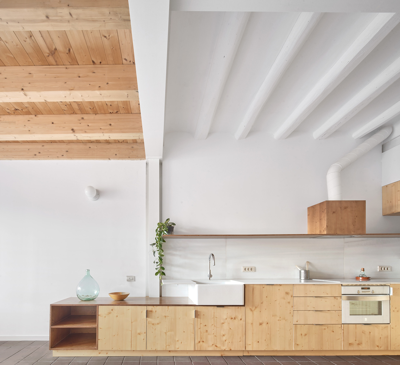 Kitchen with light pine cabinetry beneath a double-height space with exposed timber plank ceiling