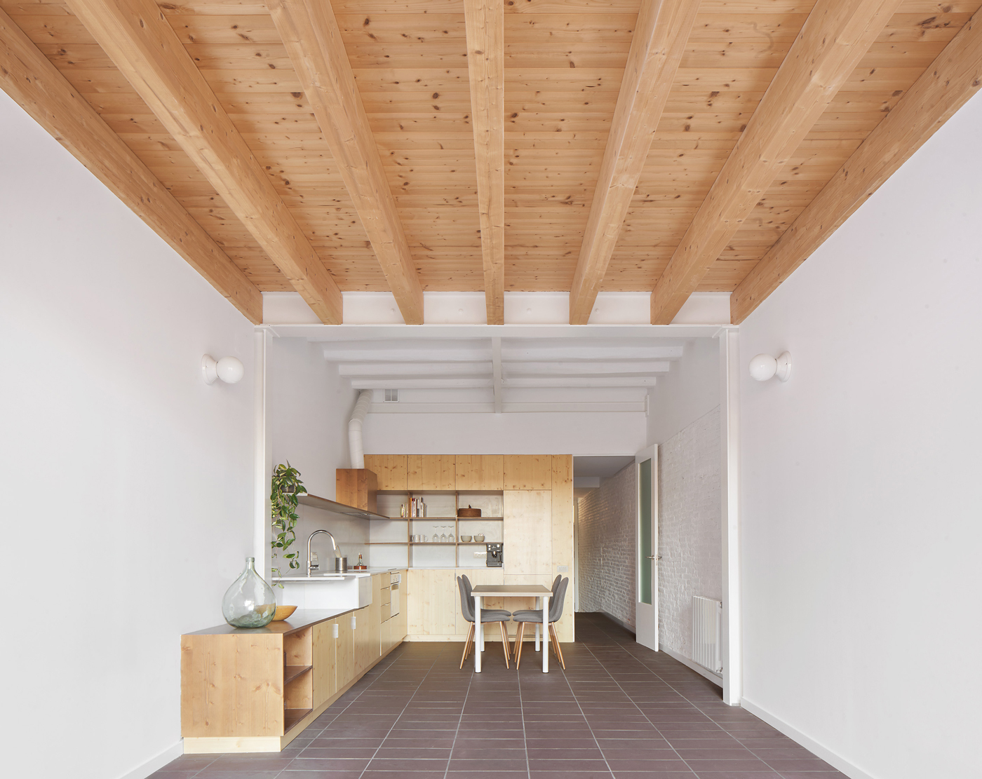 Open-plan kitchen and dining space with exposed timber beams, plywood cabinetry, and terracotta floor tiles