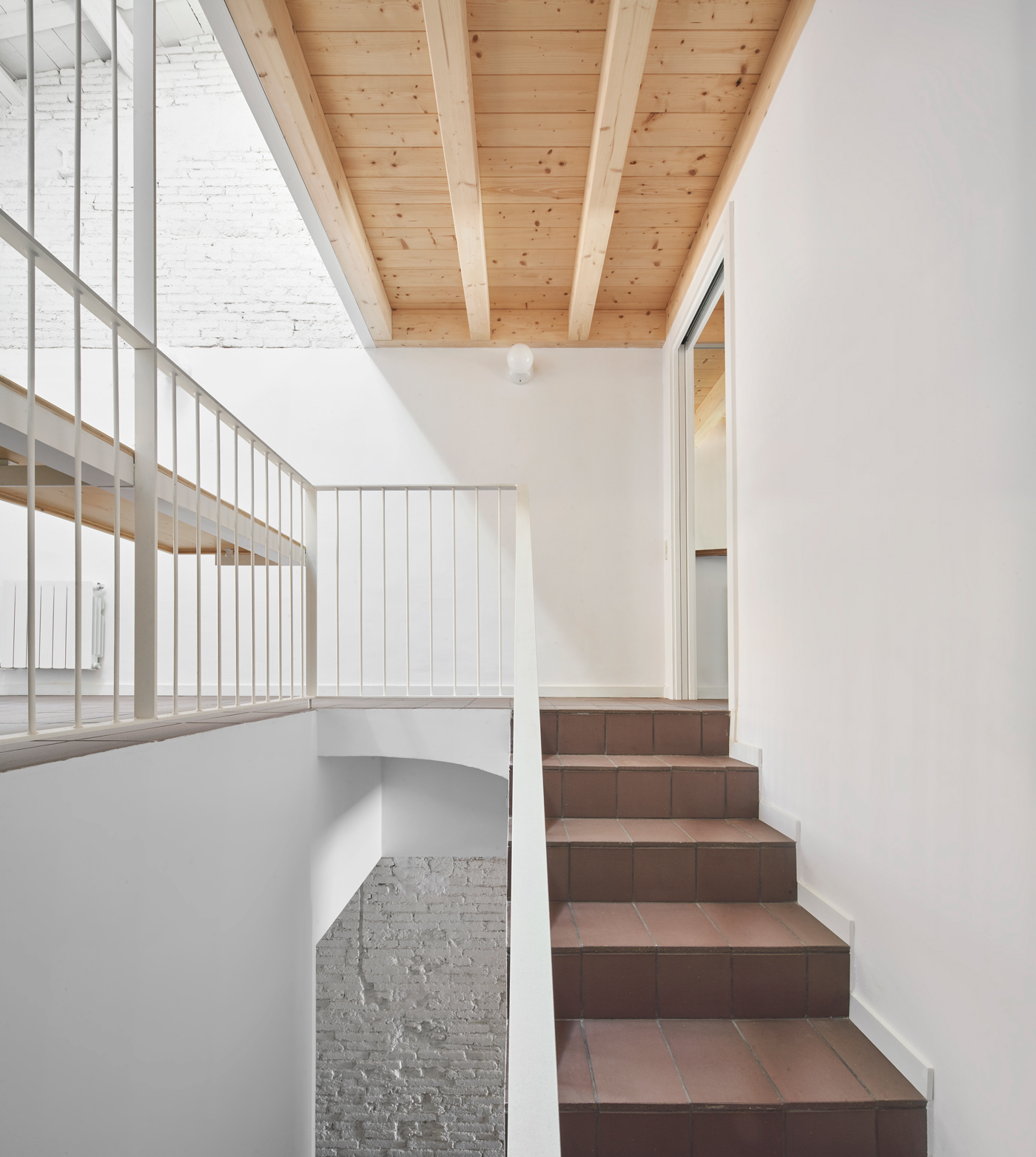 Interior staircase with terracotta treads and white metal railing beneath an exposed timber beam ceiling