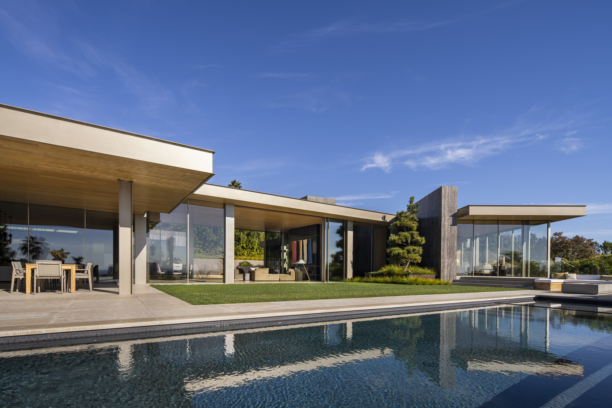 Garden facade with extended roof overhangs and glass walls opening to a lawn and swimming pool