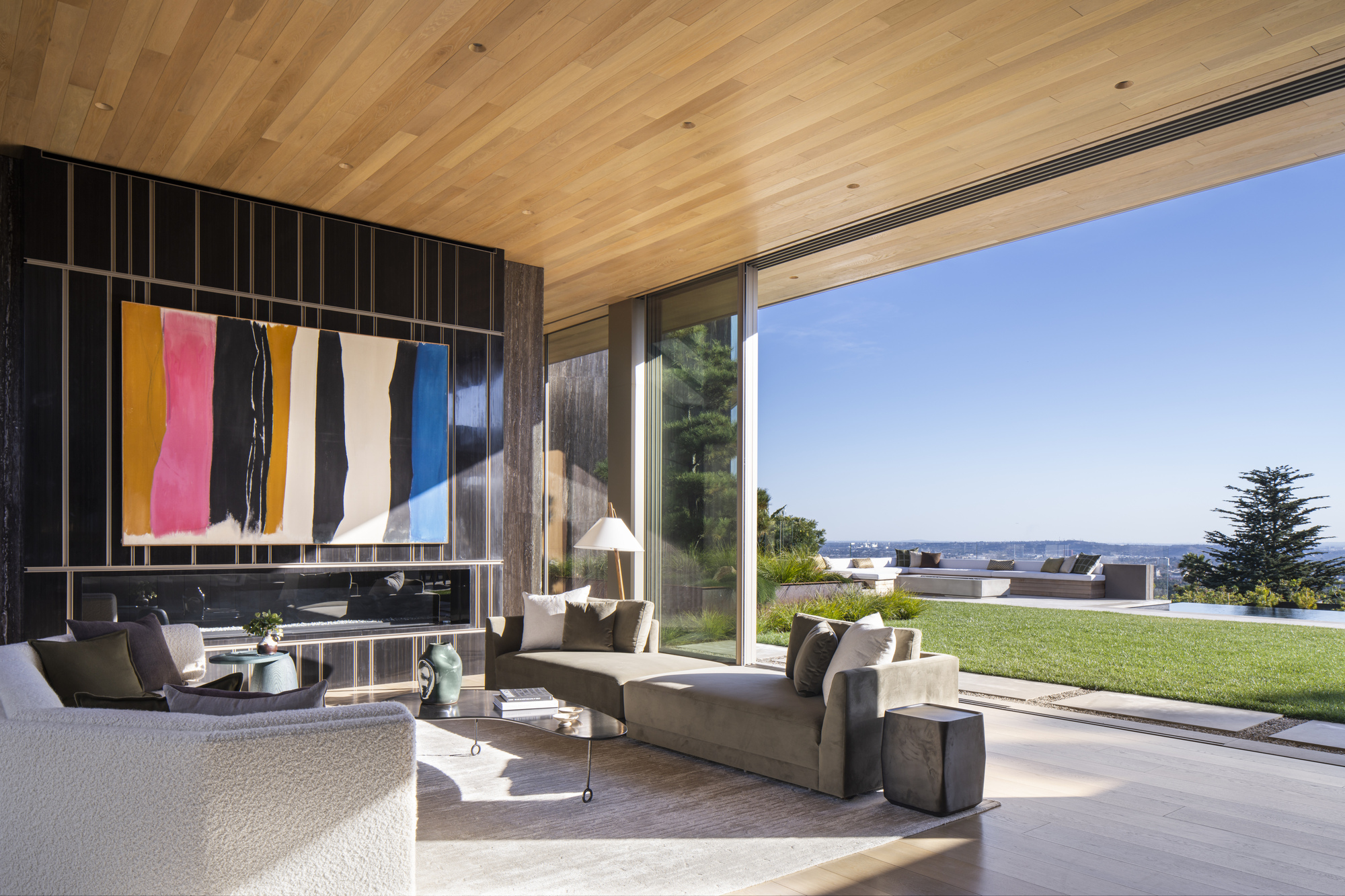 Living room with diagonal wood ceiling, dark metal wall screen, and full-height glazing to the garden