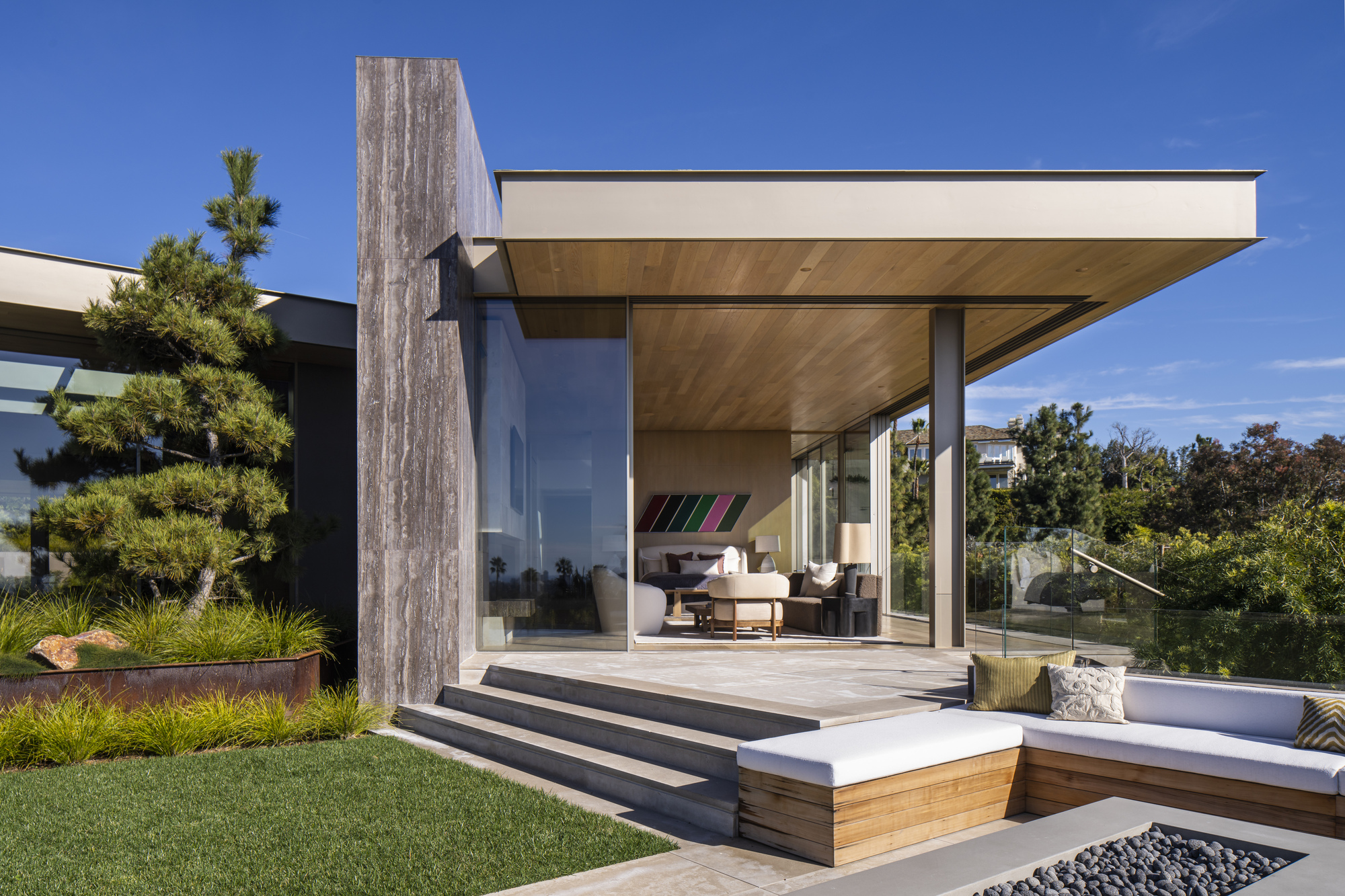 Glazed pavilion with cantilevered roof and stepped timber deck beside a sunken garden bed