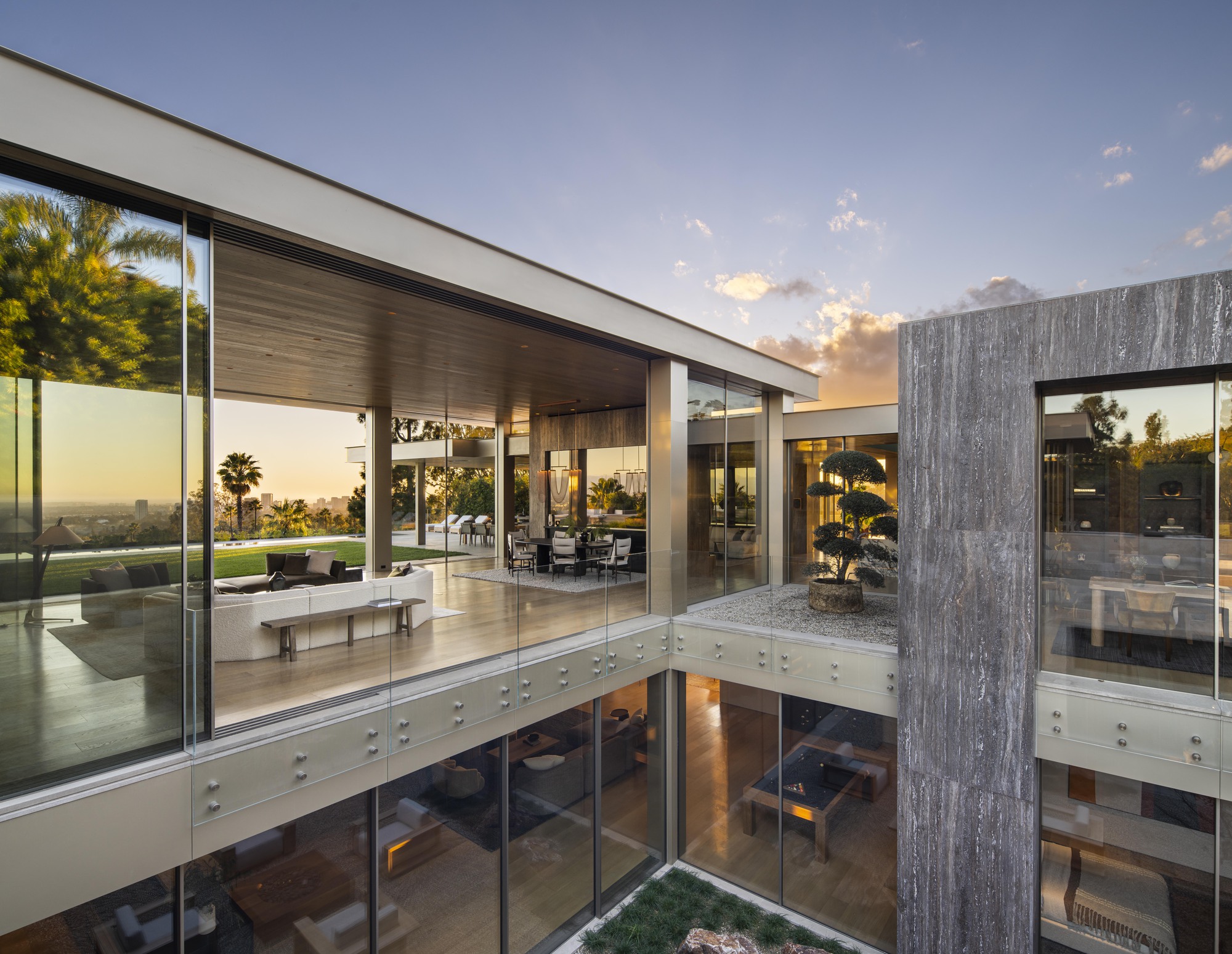 Double-height courtyard with glass-wrapped volume and weathered concrete tower at dusk