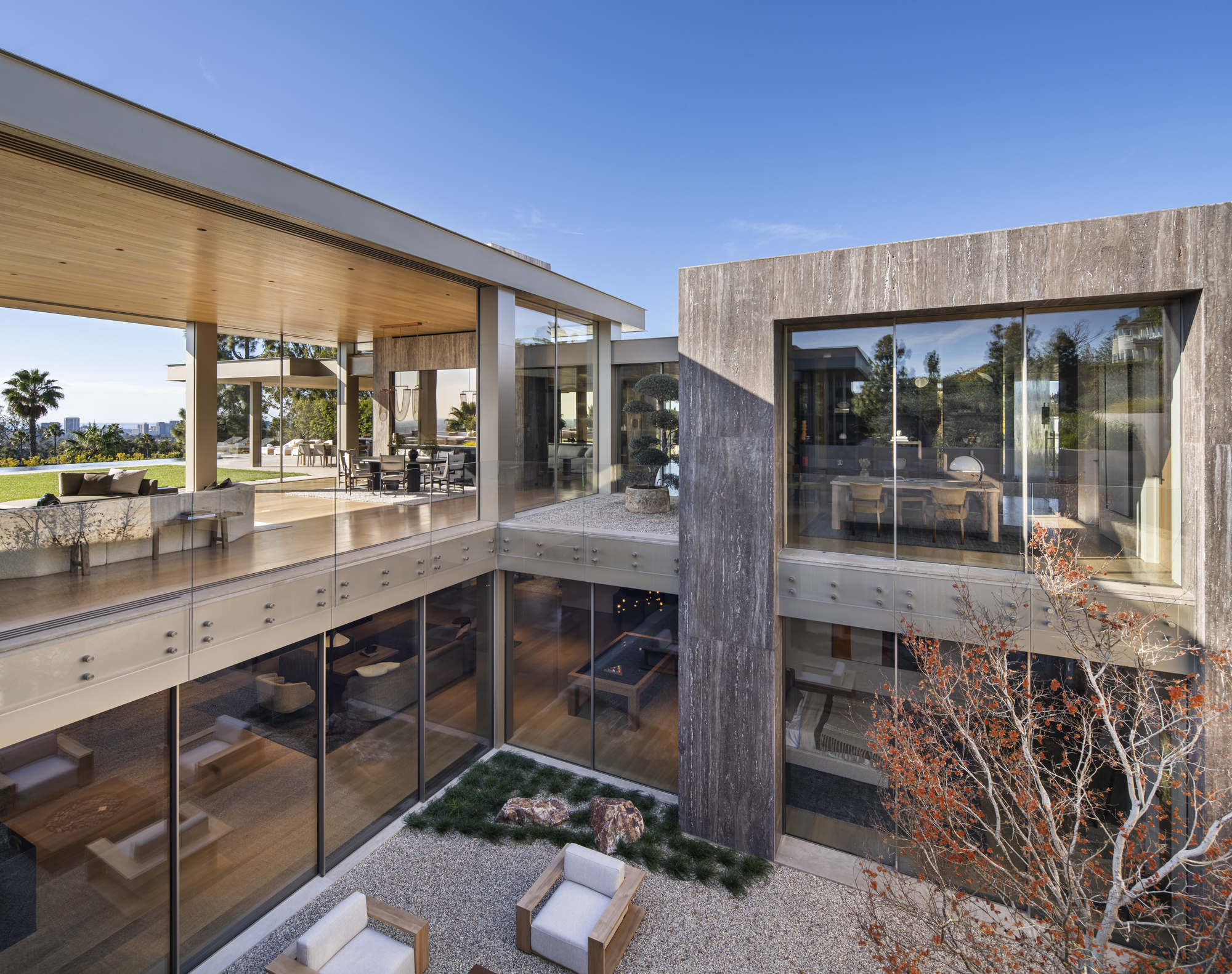 Sunken courtyard with planted bed and weathered concrete column beneath glazed upper floor terrace