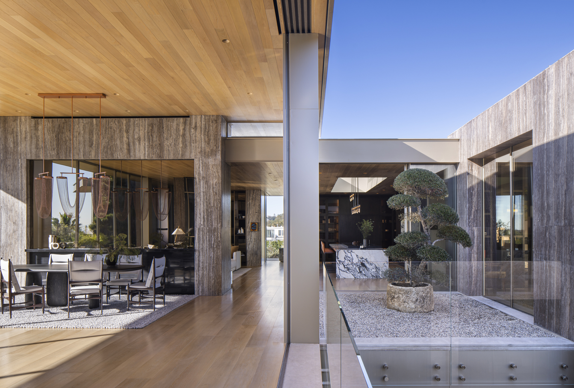 Central courtyard with gravel bed, sculptural tree in stone planter, and timber-clad volumes surrounding it