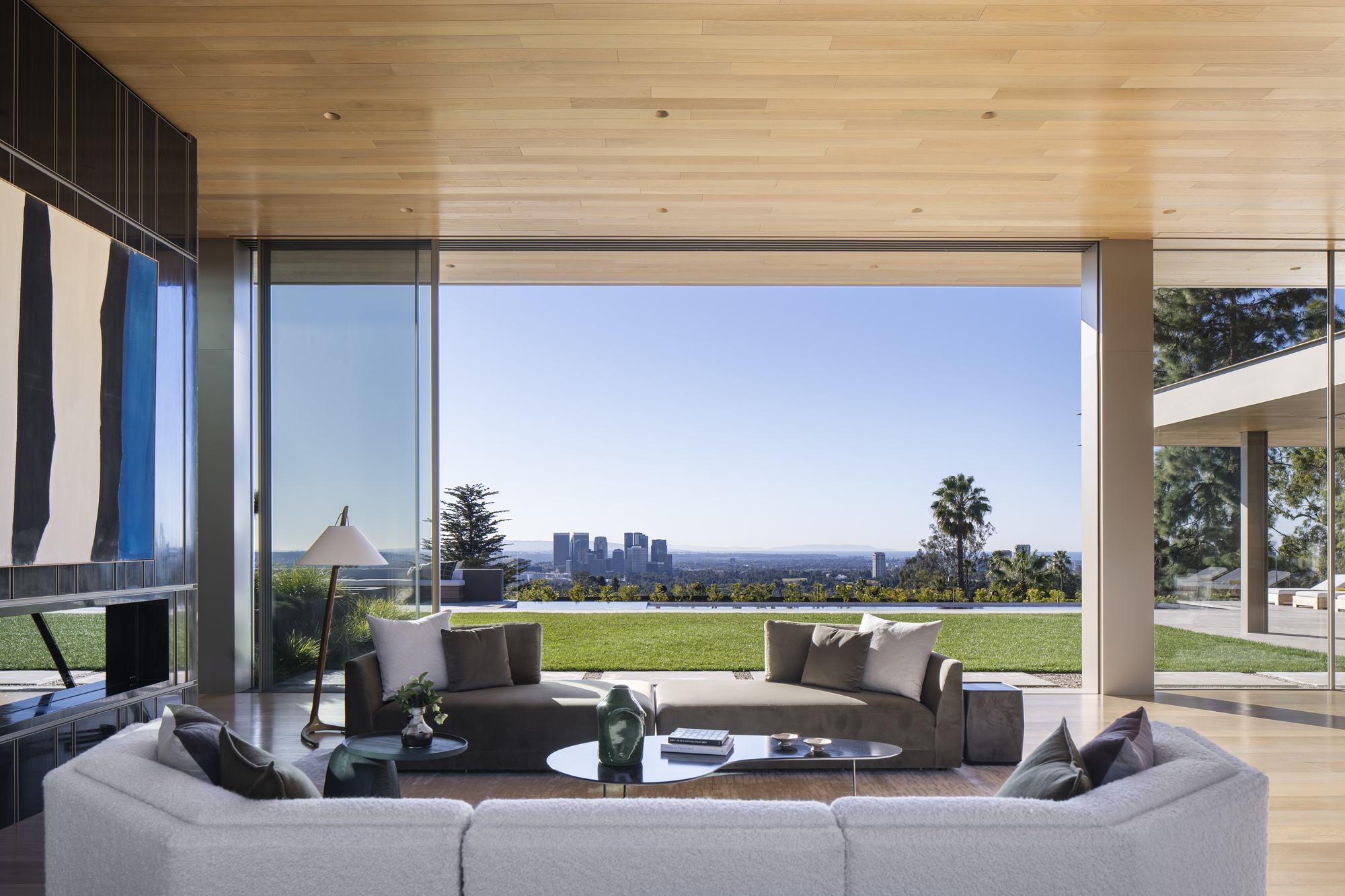 Living room with corner glazing framing lawn and distant skyline view beyond curved seating