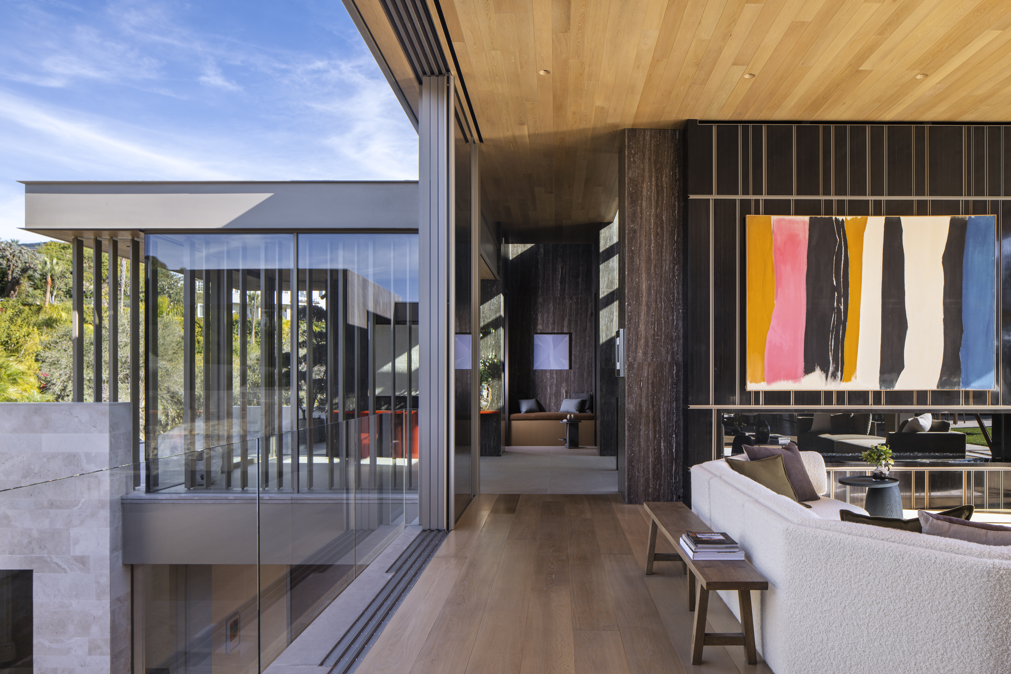 Interior view through timber-clad corridor toward cantilevered glass pavilion and vertical louvres outside