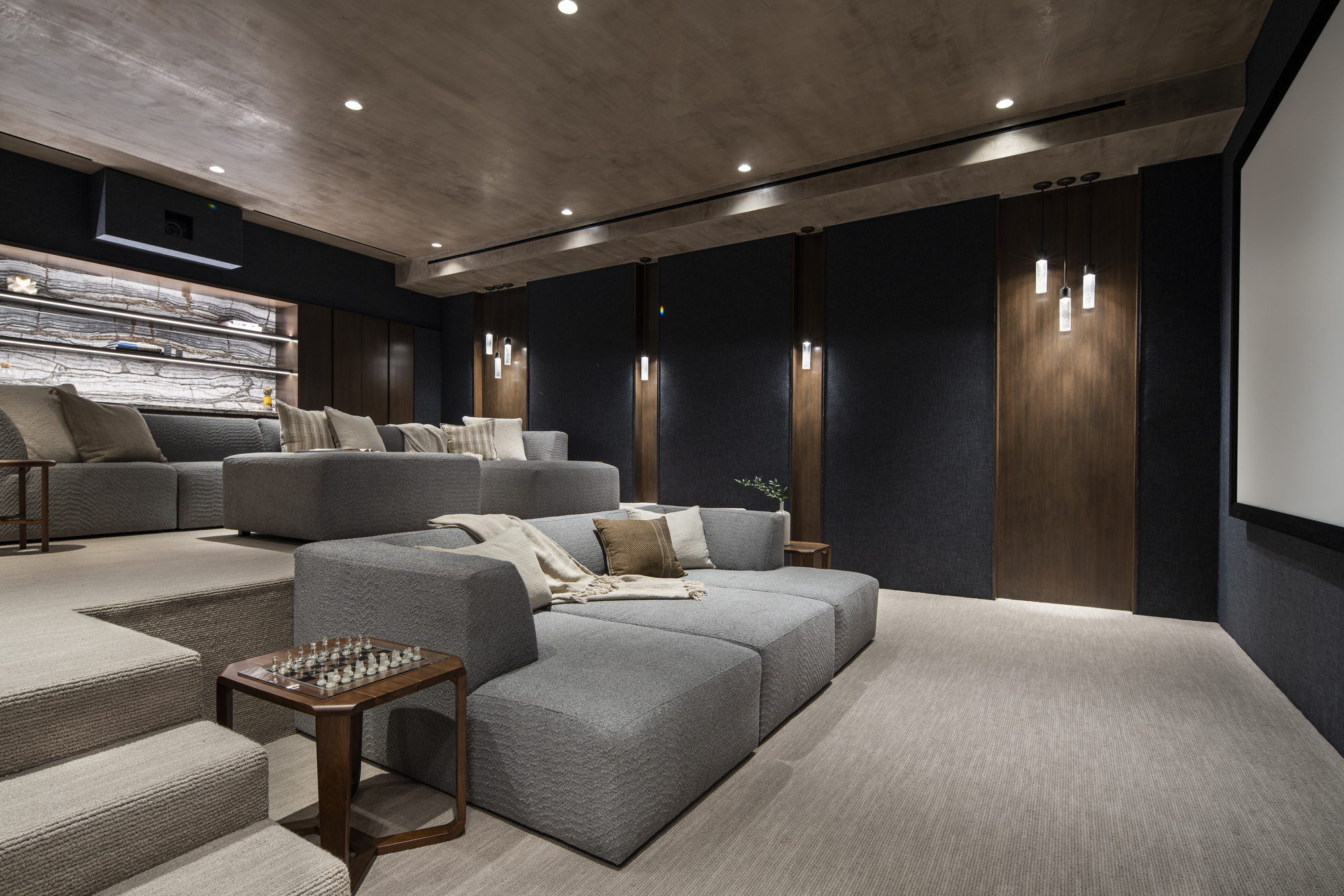 Screening room with tiered seating facing a projection wall under a textured concrete ceiling