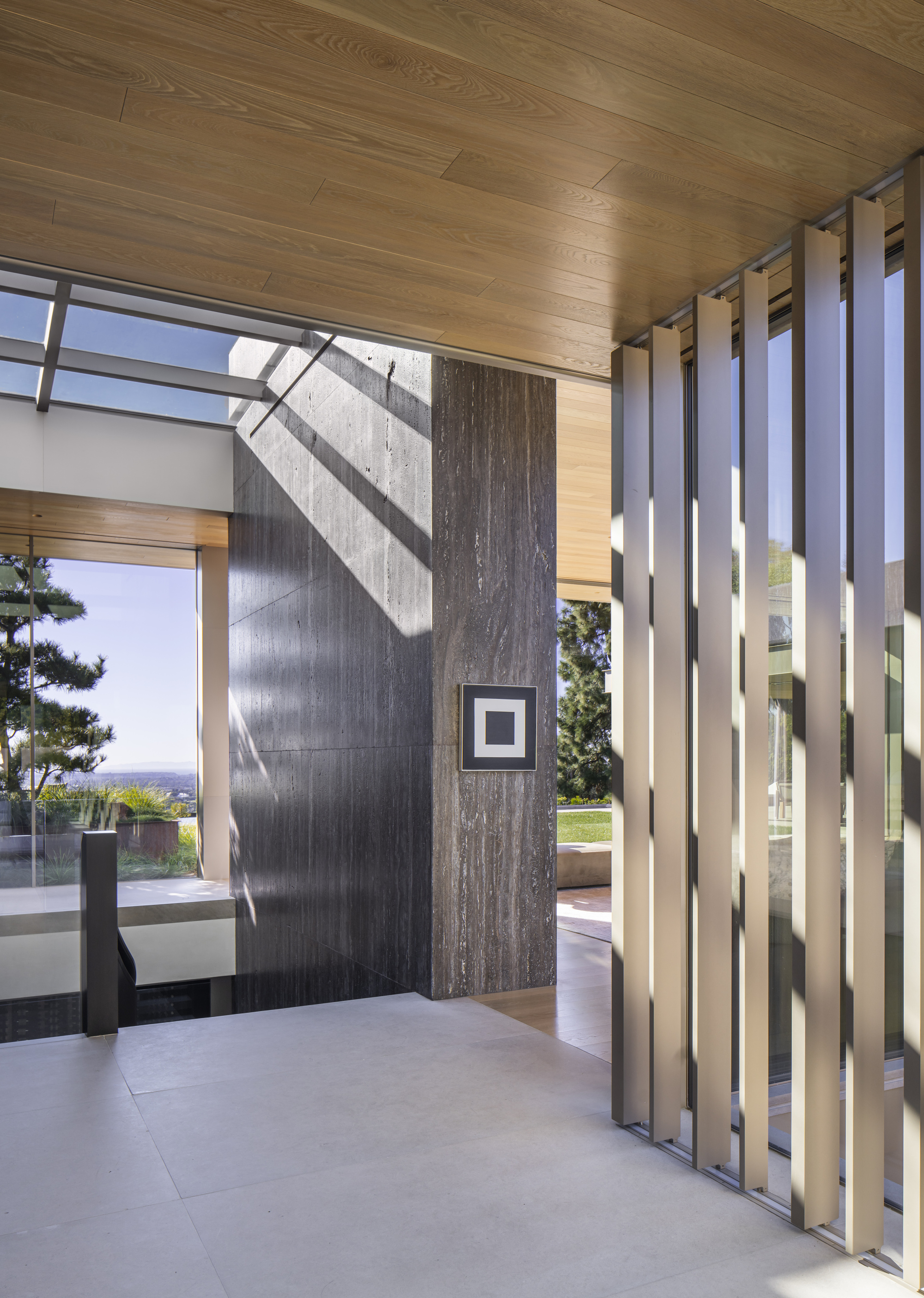 Entry threshold with vertical metal screen and board-formed concrete pivot wall casting shadows in daylight