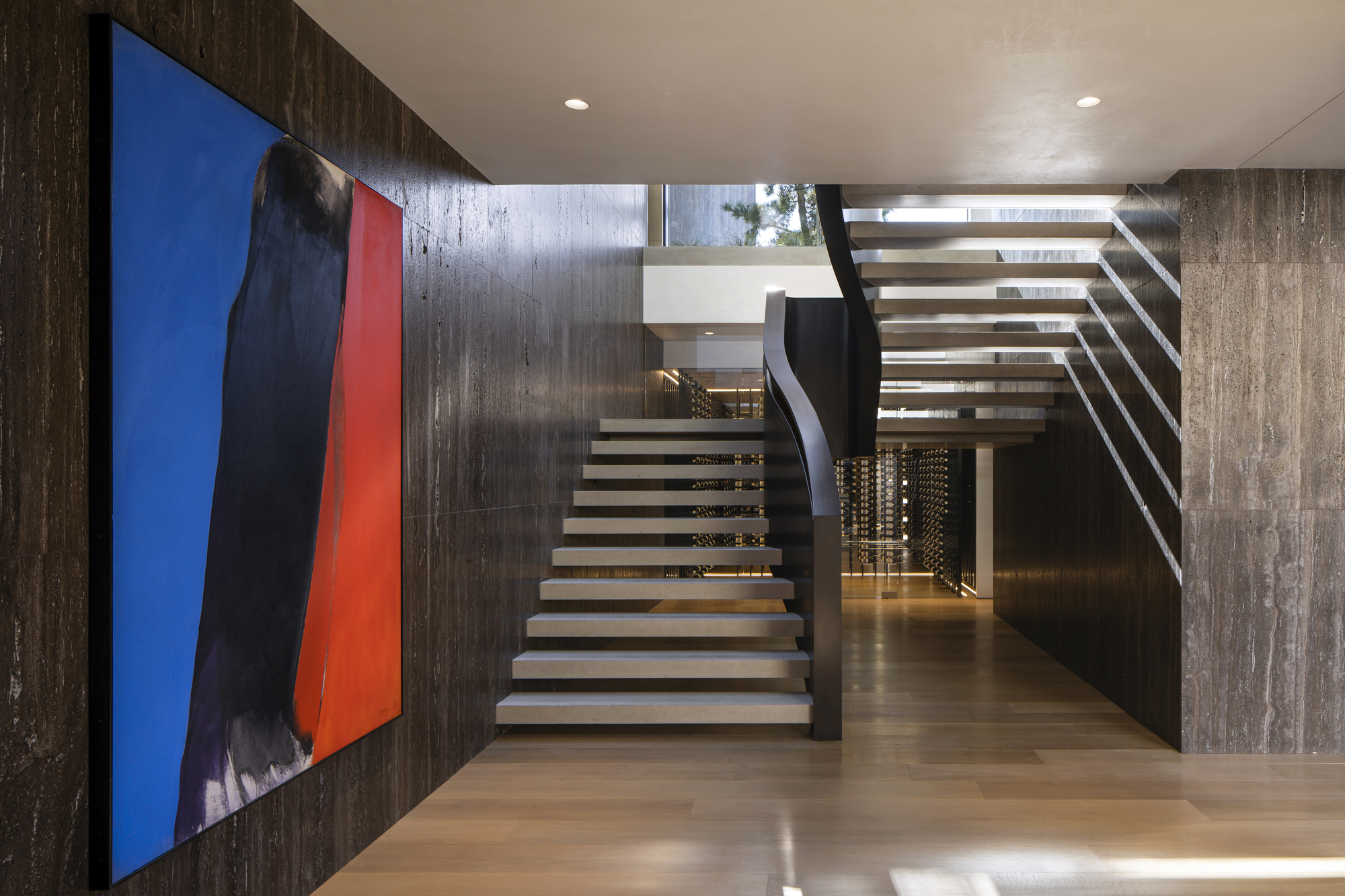 Open-tread staircase with steel stringers ascending beside a board-formed concrete wall and colorful canvas