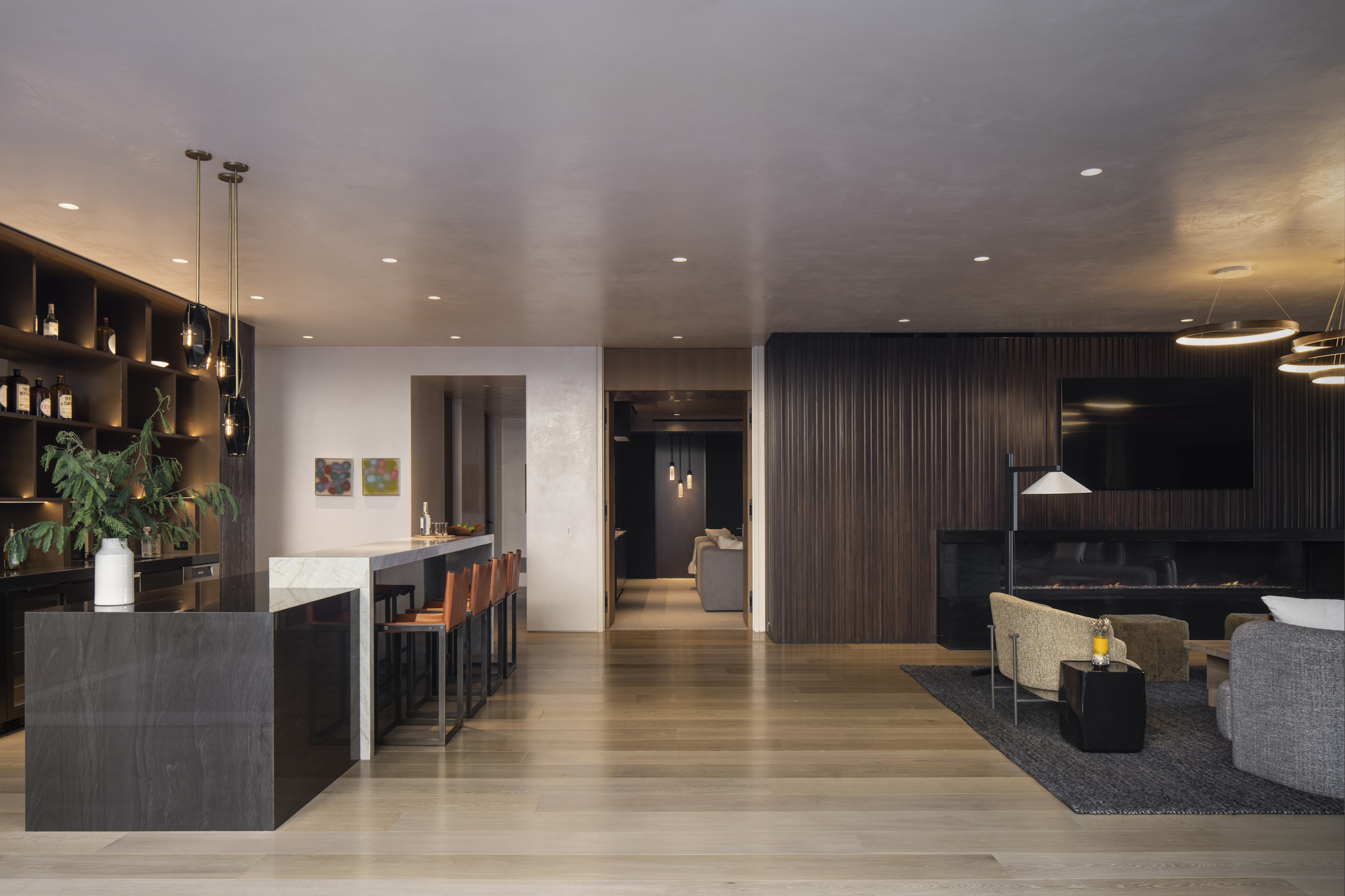 Open-plan living area with dark wood wall panels, stone bar island, and recessed ceiling lighting