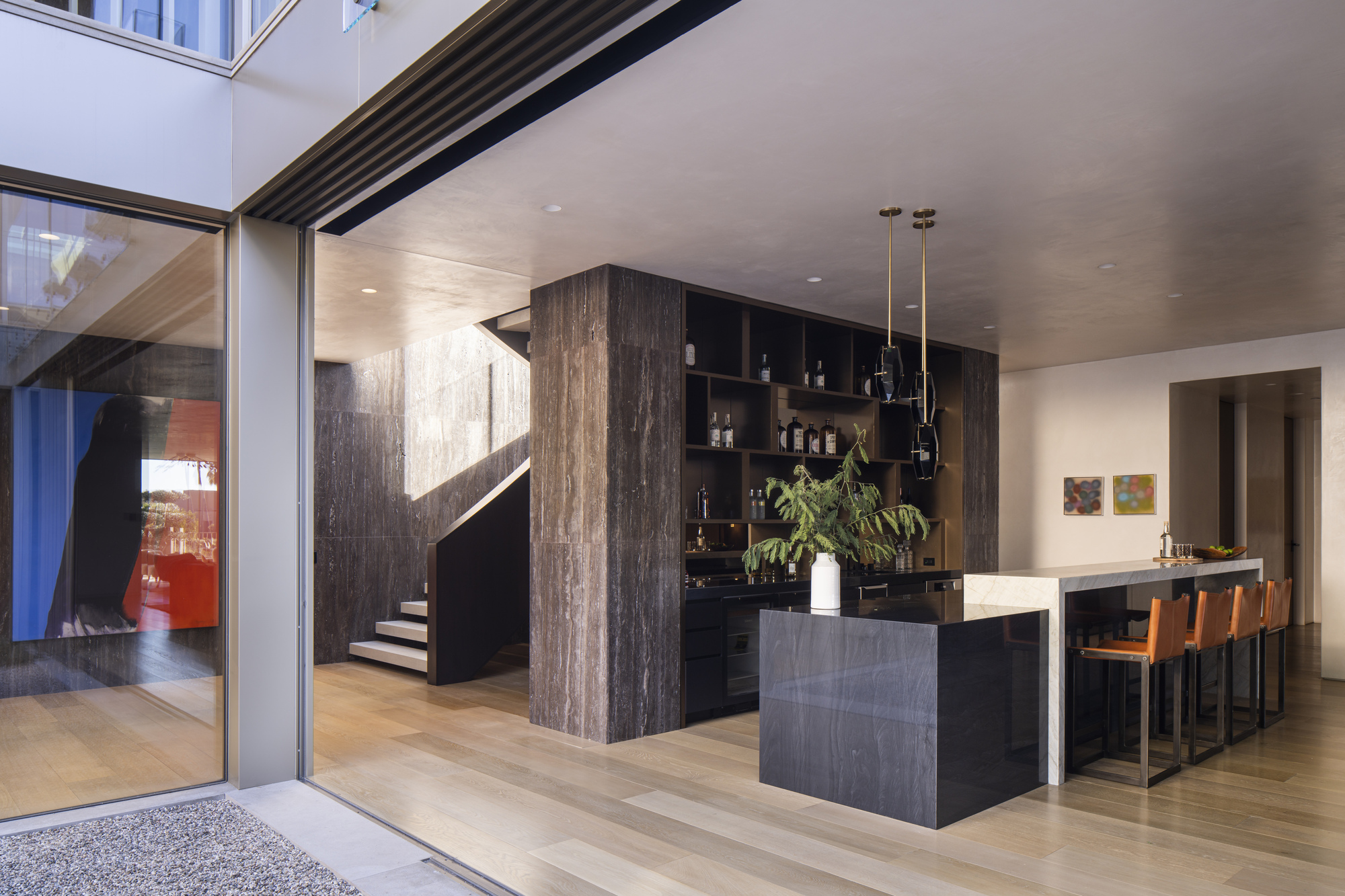 View from exterior threshold showing kitchen bar, sculptural staircase, and full-height glazed sliding doors