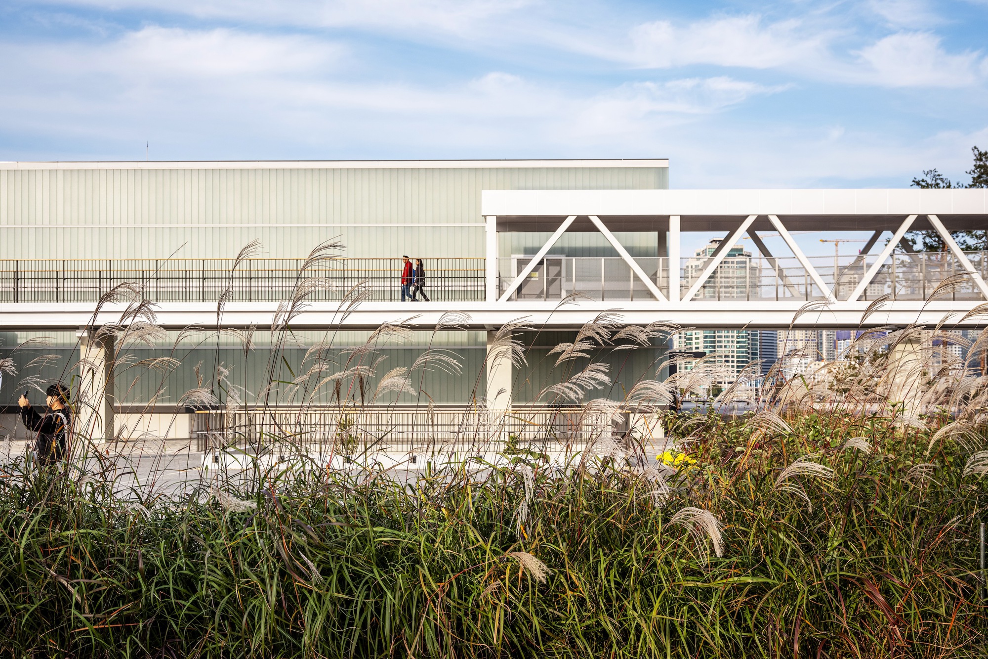 White truss bridge crossing above the corrugated metal building with ornamental grasses in the foreground