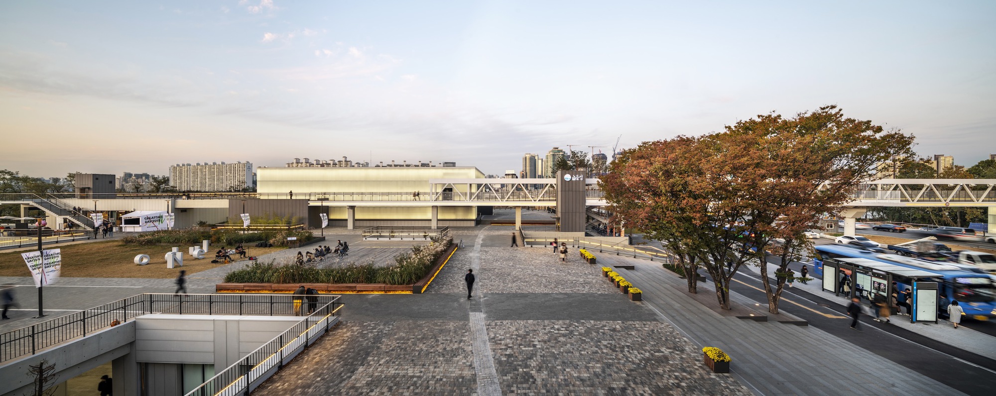 Public plaza with cobblestone paving and an autumn tree between raised transit platforms