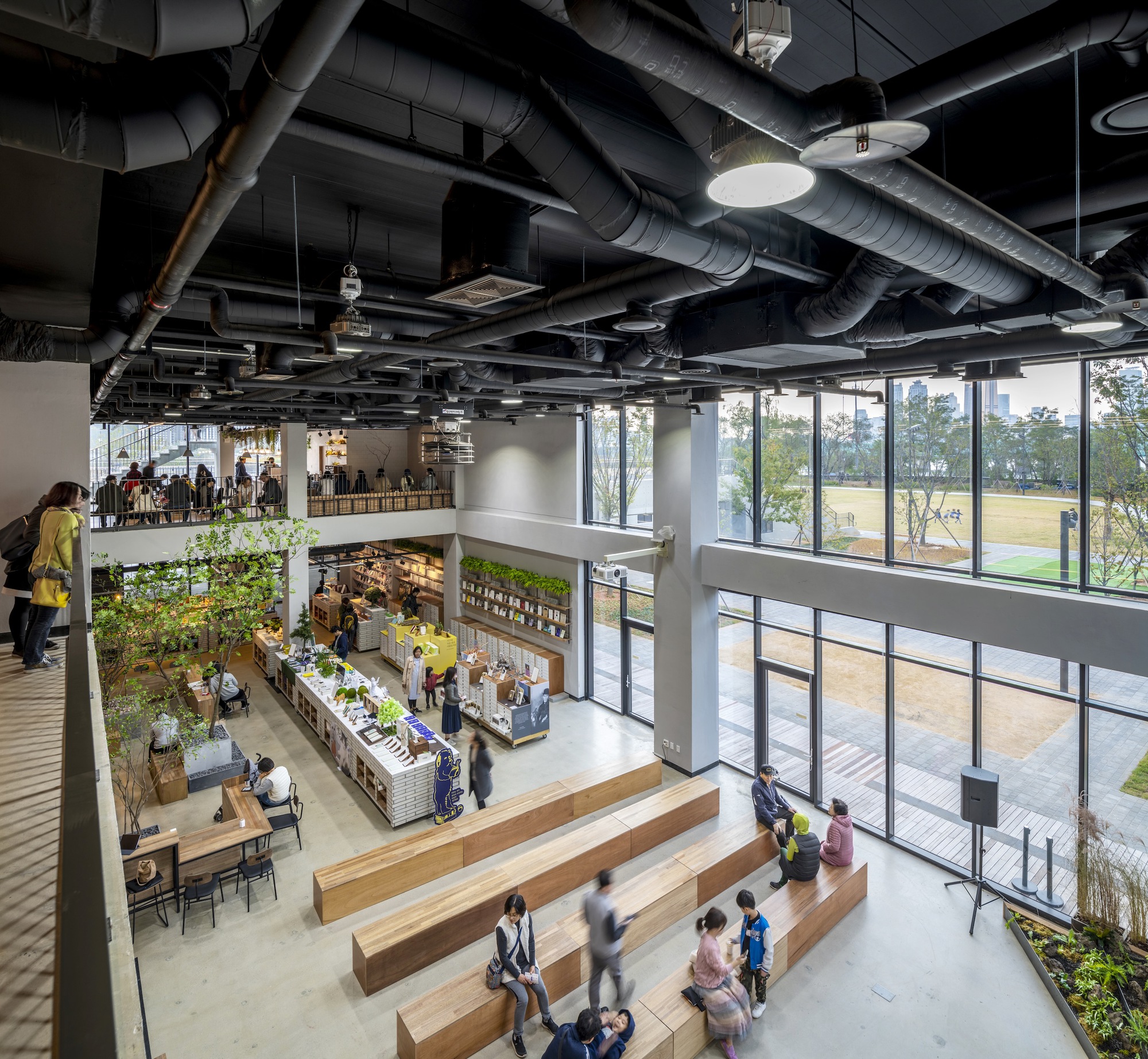 Double-height interior marketplace with timber stepped seating and exposed mechanical systems above