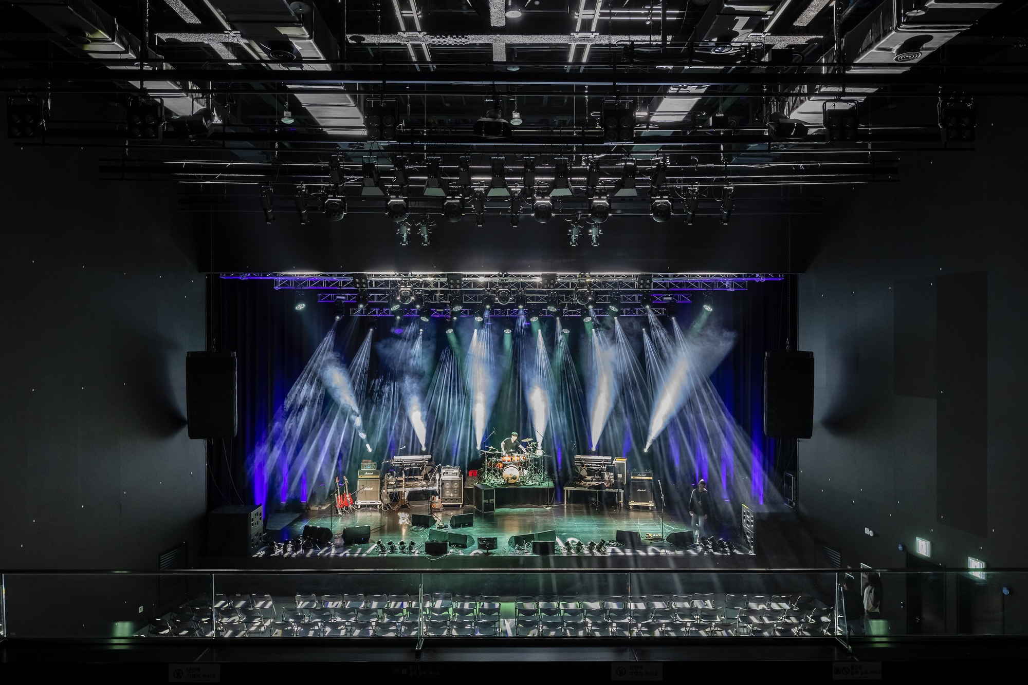Performance stage rigged with theatrical lighting under a dense grid of exposed mechanical and electrical systems