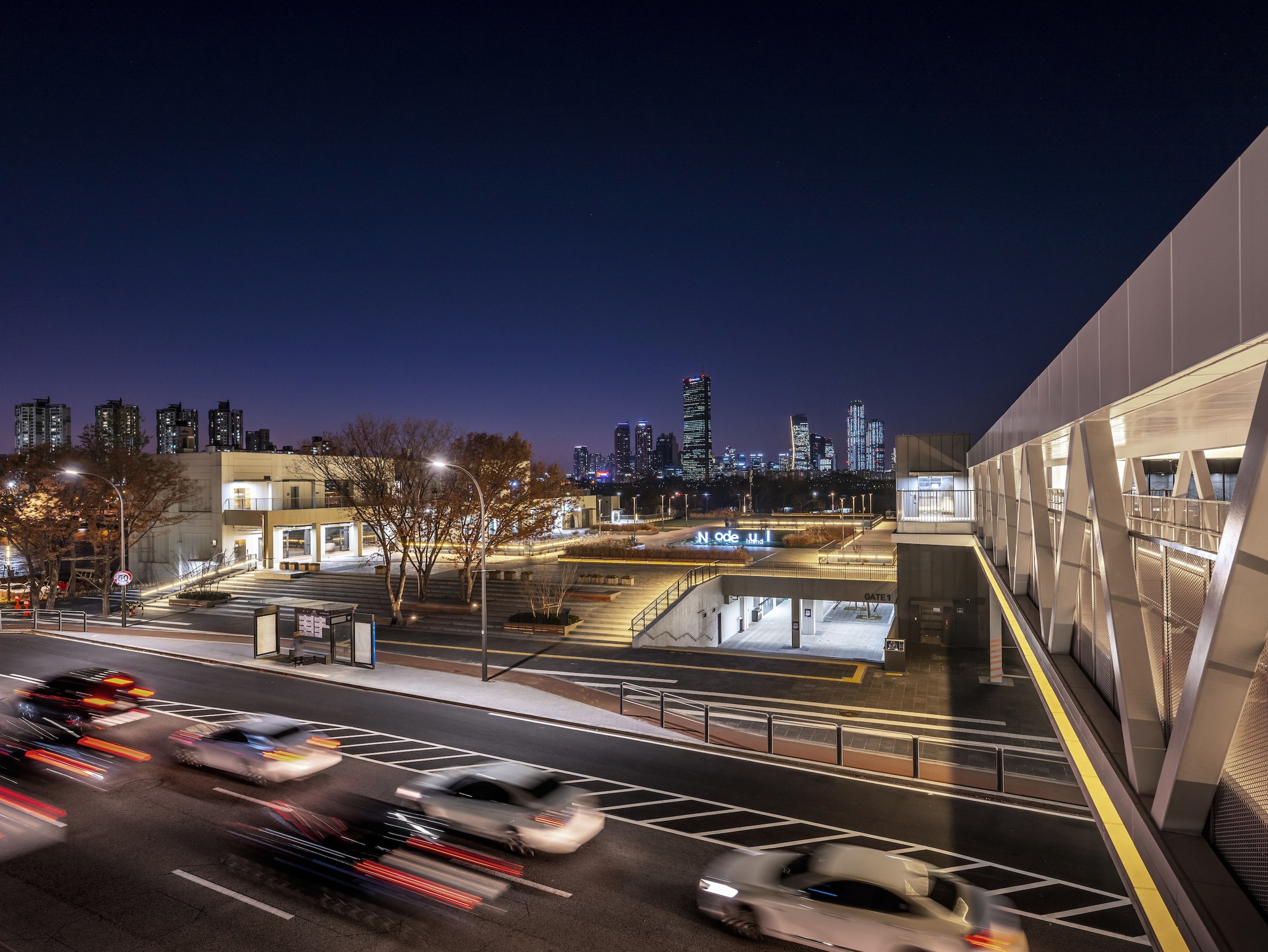 Aerial view of the pedestrian bridge and sunken plaza with city skyline at dusk