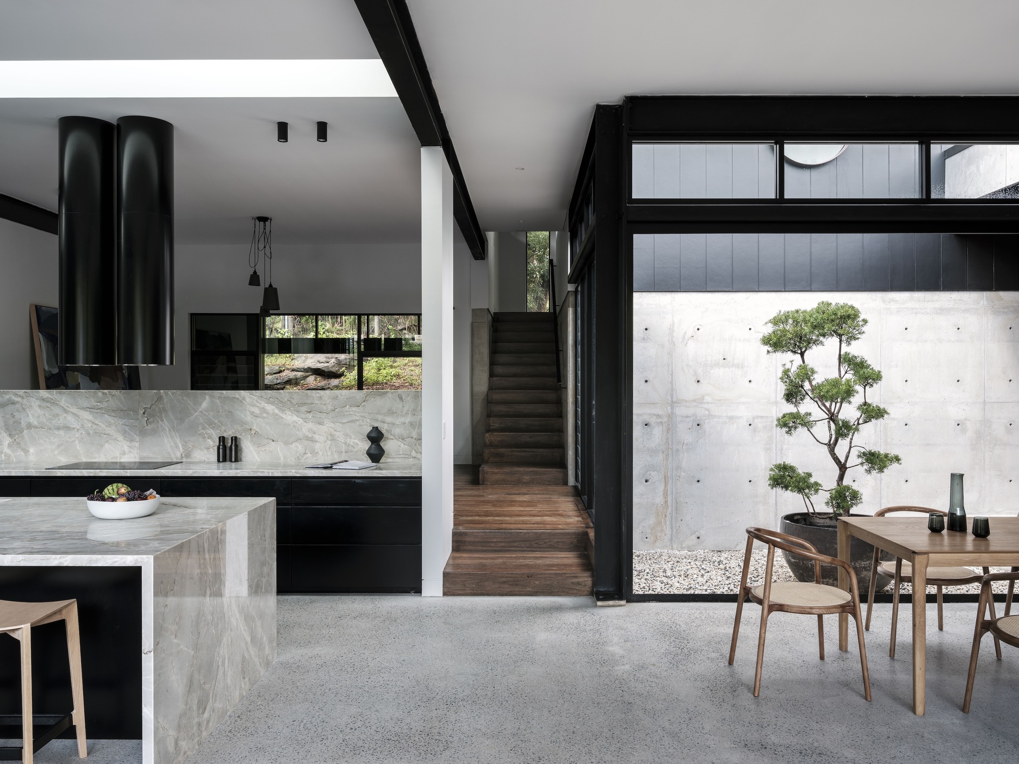 Open-plan kitchen and dining area with marble island, black cabinetry, and courtyard view with bonsai tree