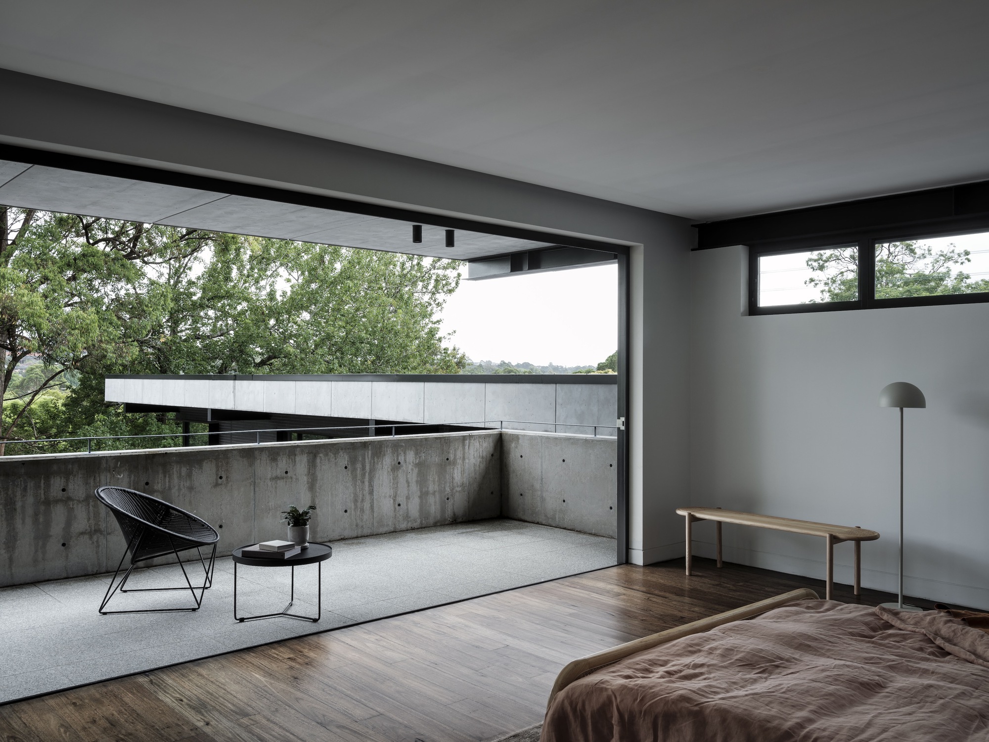 Bedroom opening to concrete terrace with wire chair overlooking leafy canopy