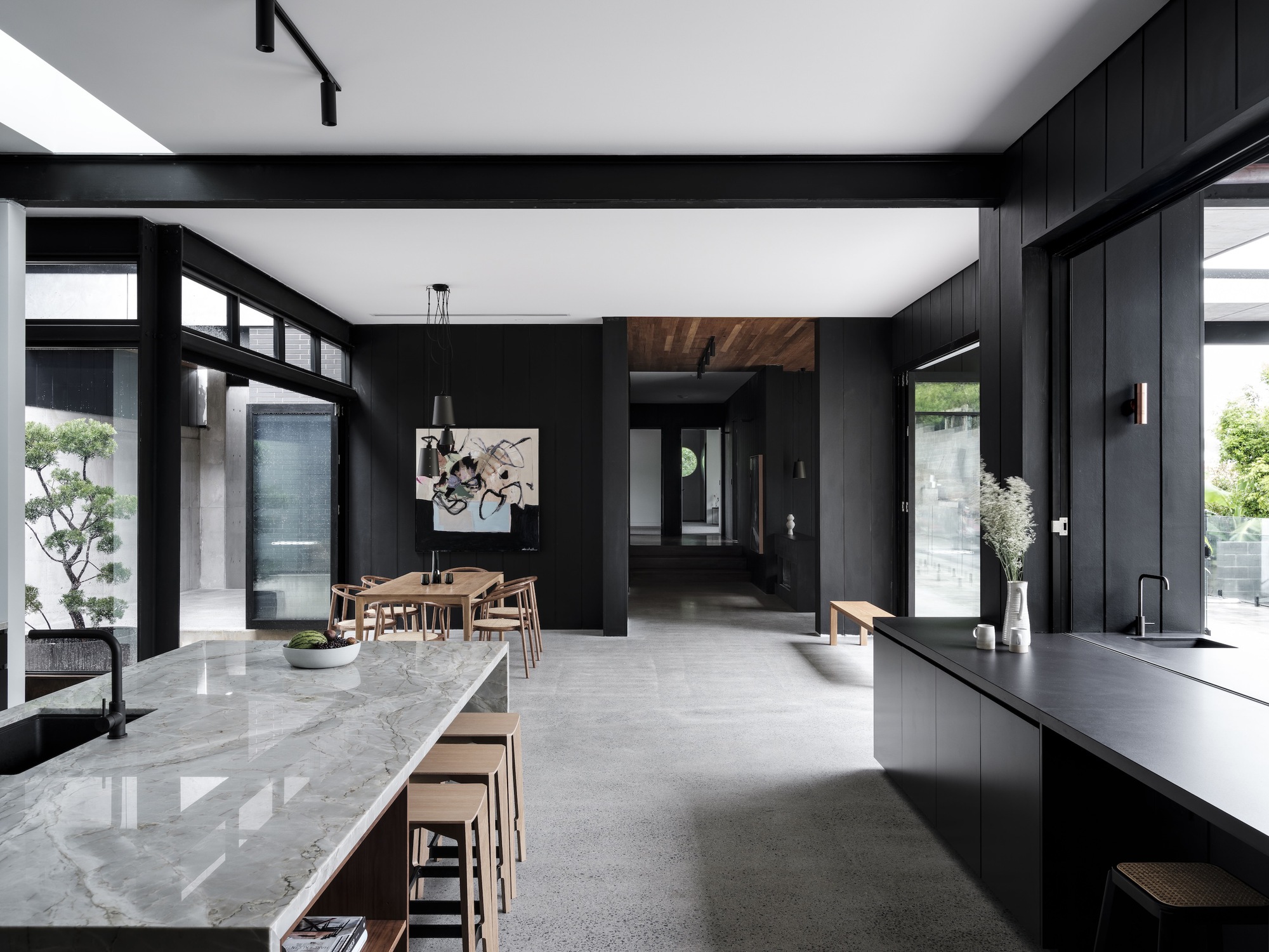 Open-plan kitchen and dining area with black timber walls, marble island, and high clerestory windows