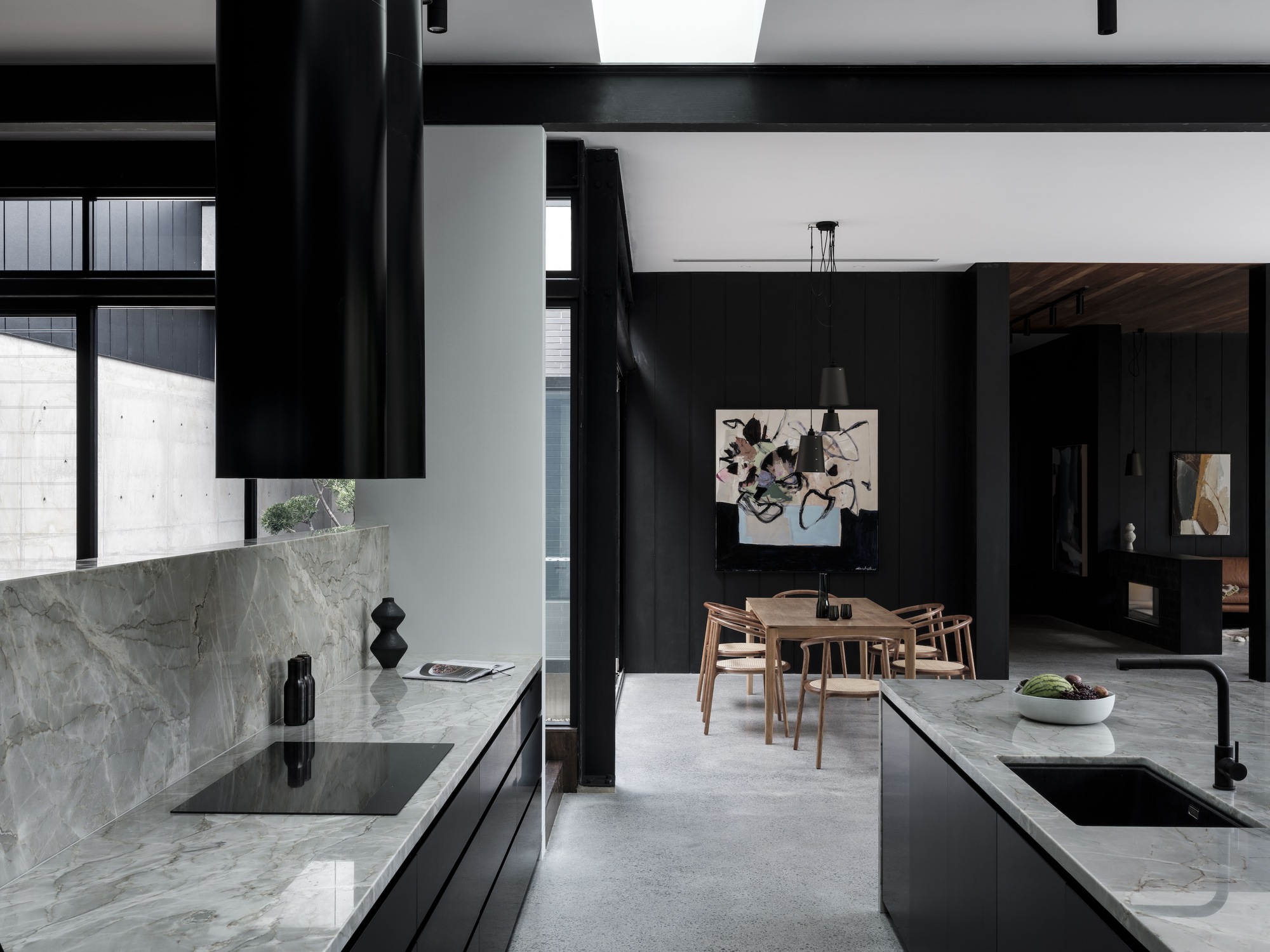 Kitchen island with grey marble countertop and timber dining table visible through black structural columns