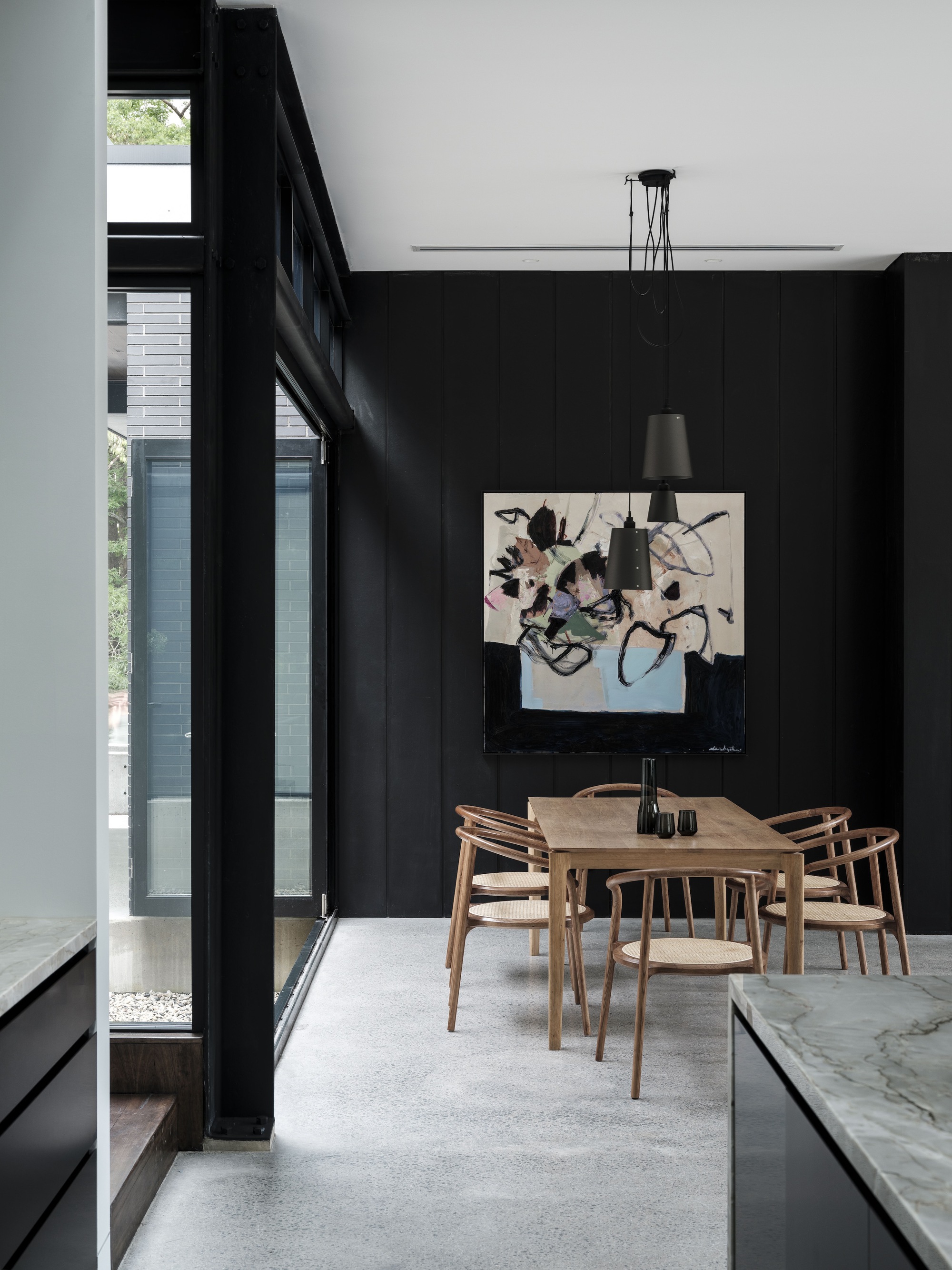 Timber dining table centered beneath black pendant lights with full-height glazing on left wall