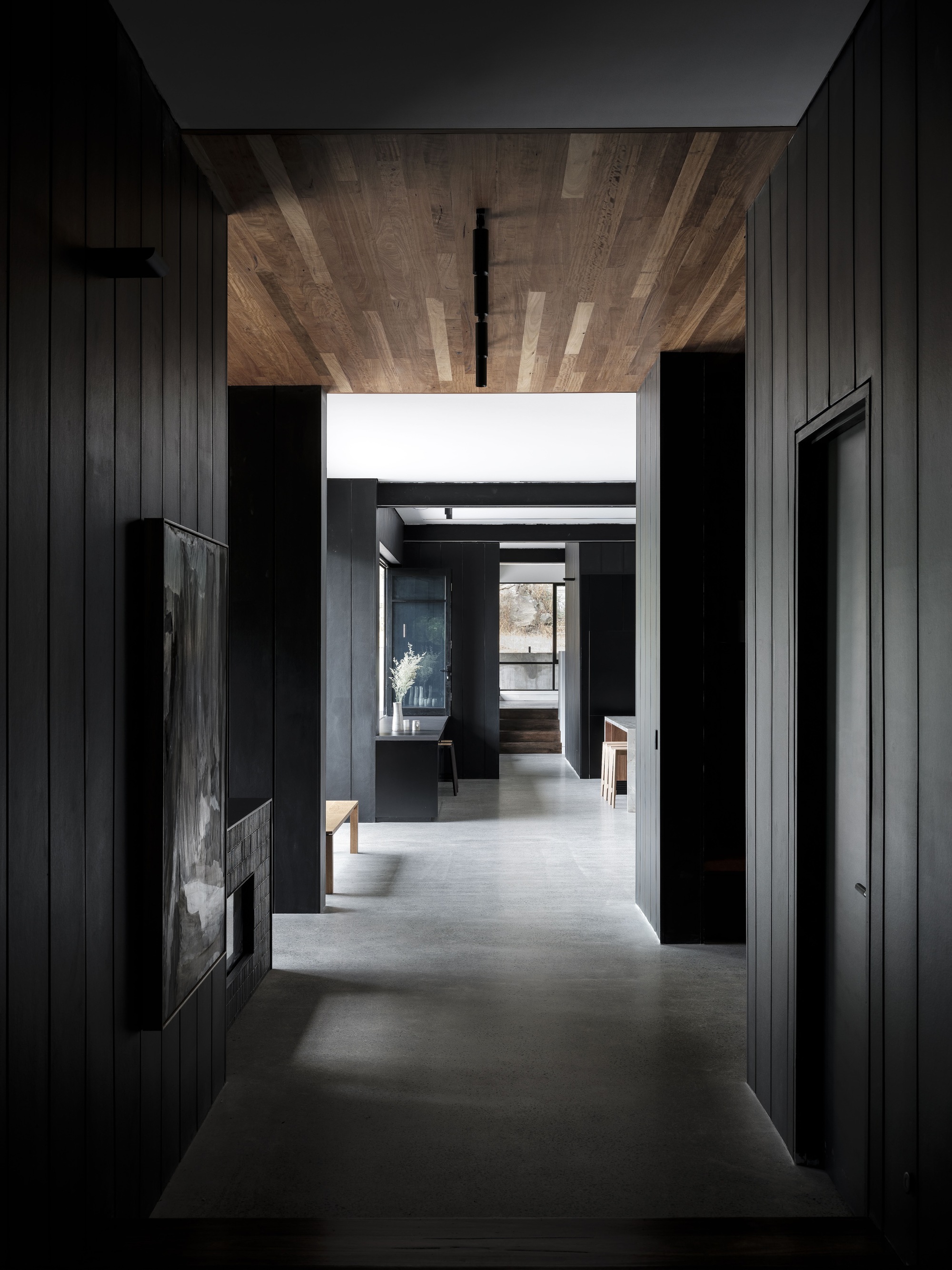 Corridor with timber plank ceiling stretching toward glazed opening with natural daylight filtering through