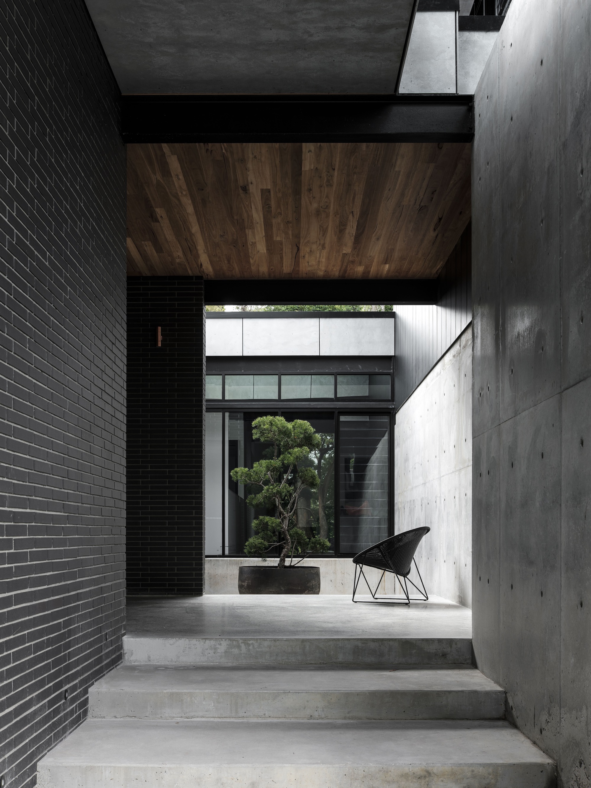 Concrete stairs ascending between black brick wall and board-formed concrete wall with timber ceiling panel overhead