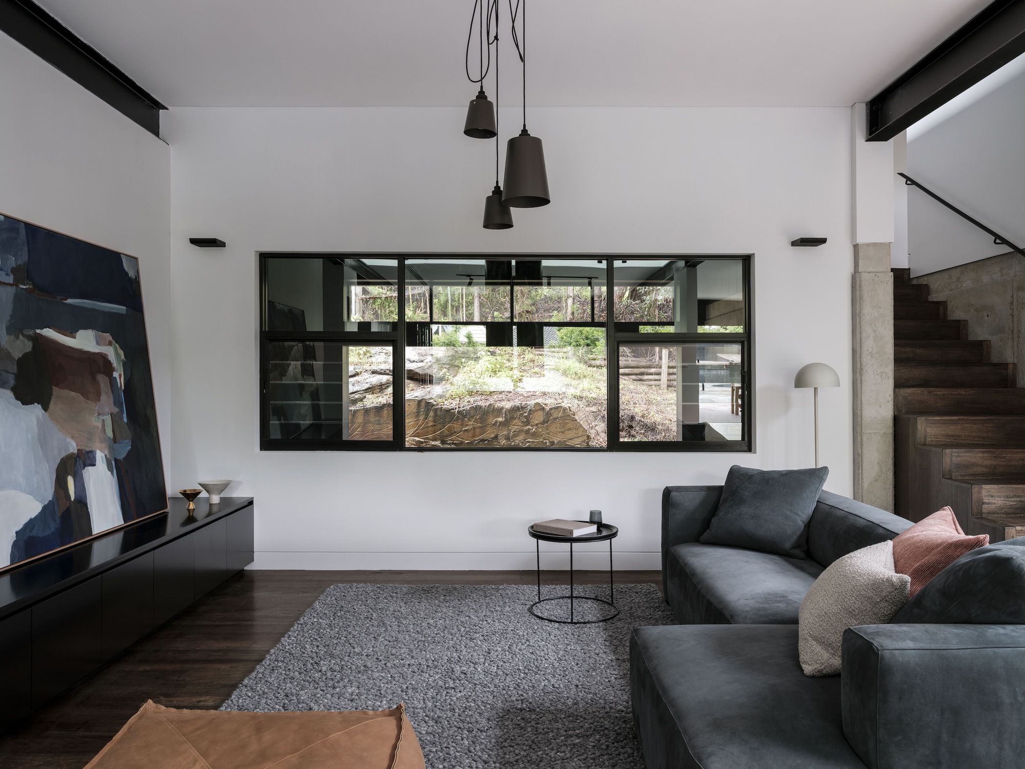 Double-height living room with black-framed window overlooking an excavated courtyard and concrete retaining wall