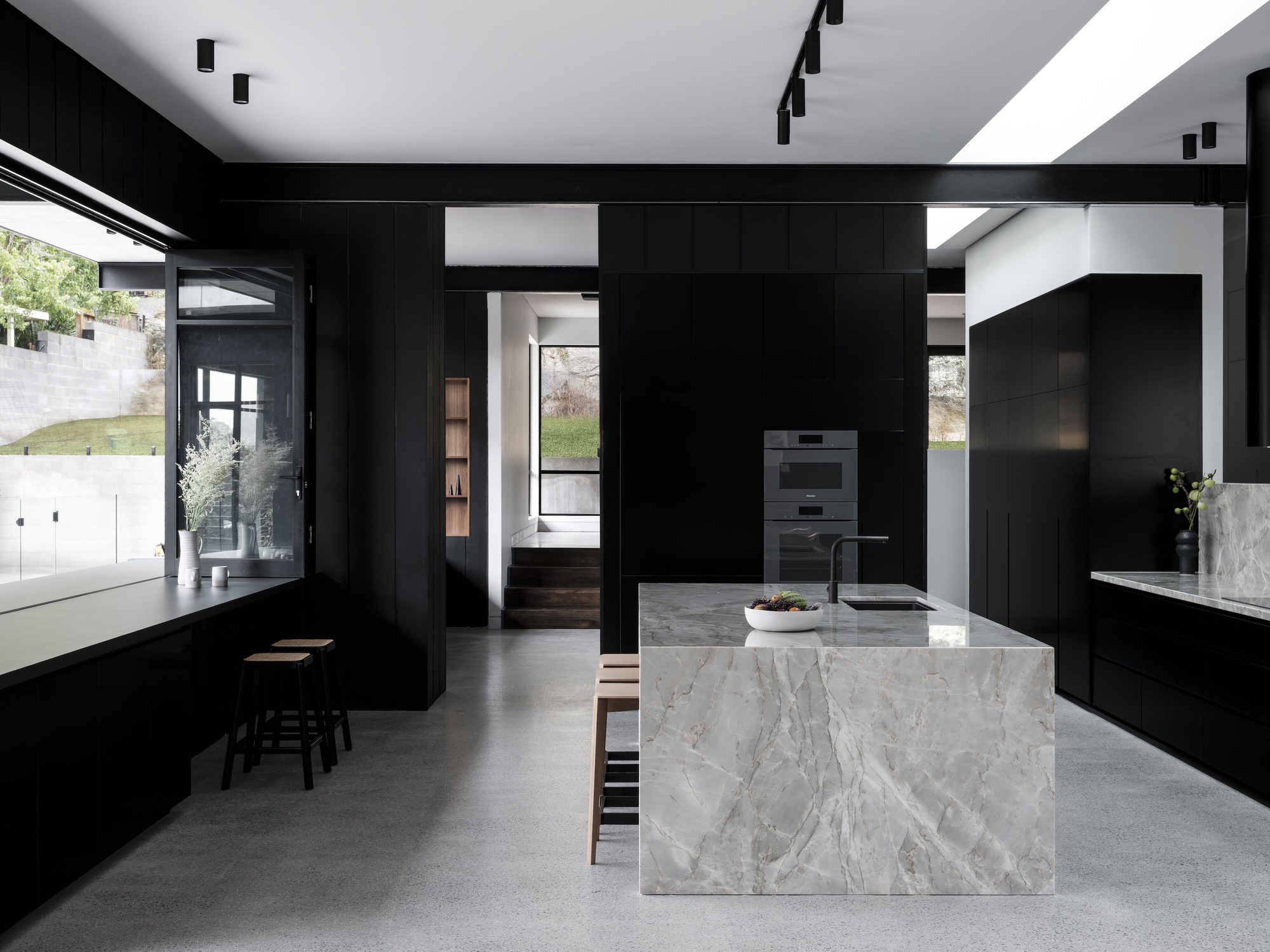 Kitchen with black paneled cabinetry and a waterfall-edge marble island under skylights