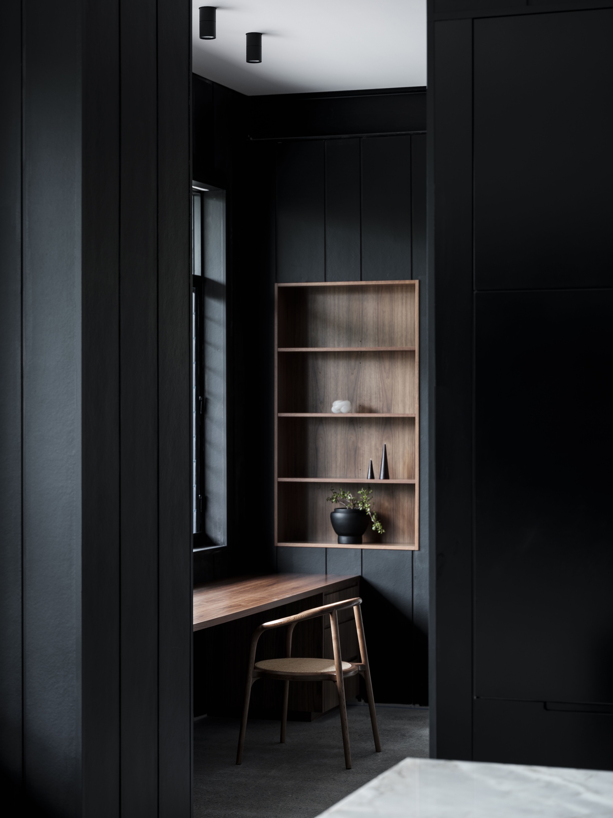 Black paneled study nook with recessed timber shelving and floating desk beneath a white ceiling