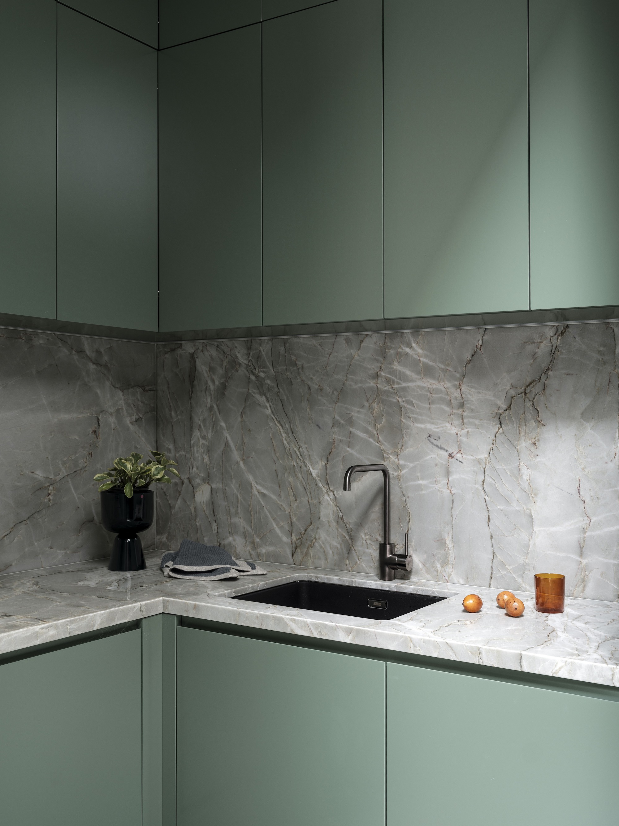 Corner kitchen with sage green cabinetry and grey veined marble backsplash and countertop