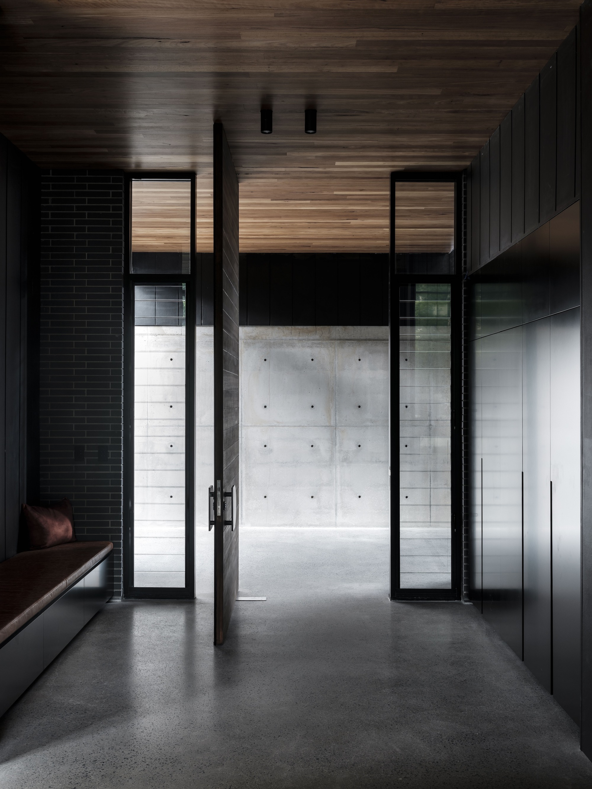 Glass door opening from timber-clad interior hallway to concrete courtyard beyond