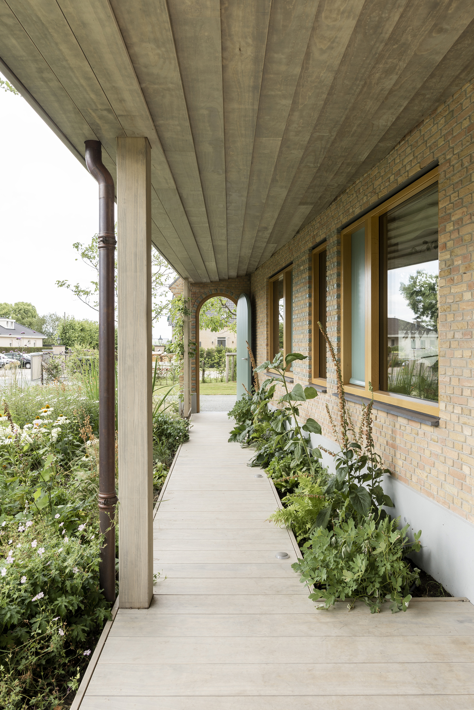 Covered walkway with concrete plank ceiling alongside planted bed and brick wall windows